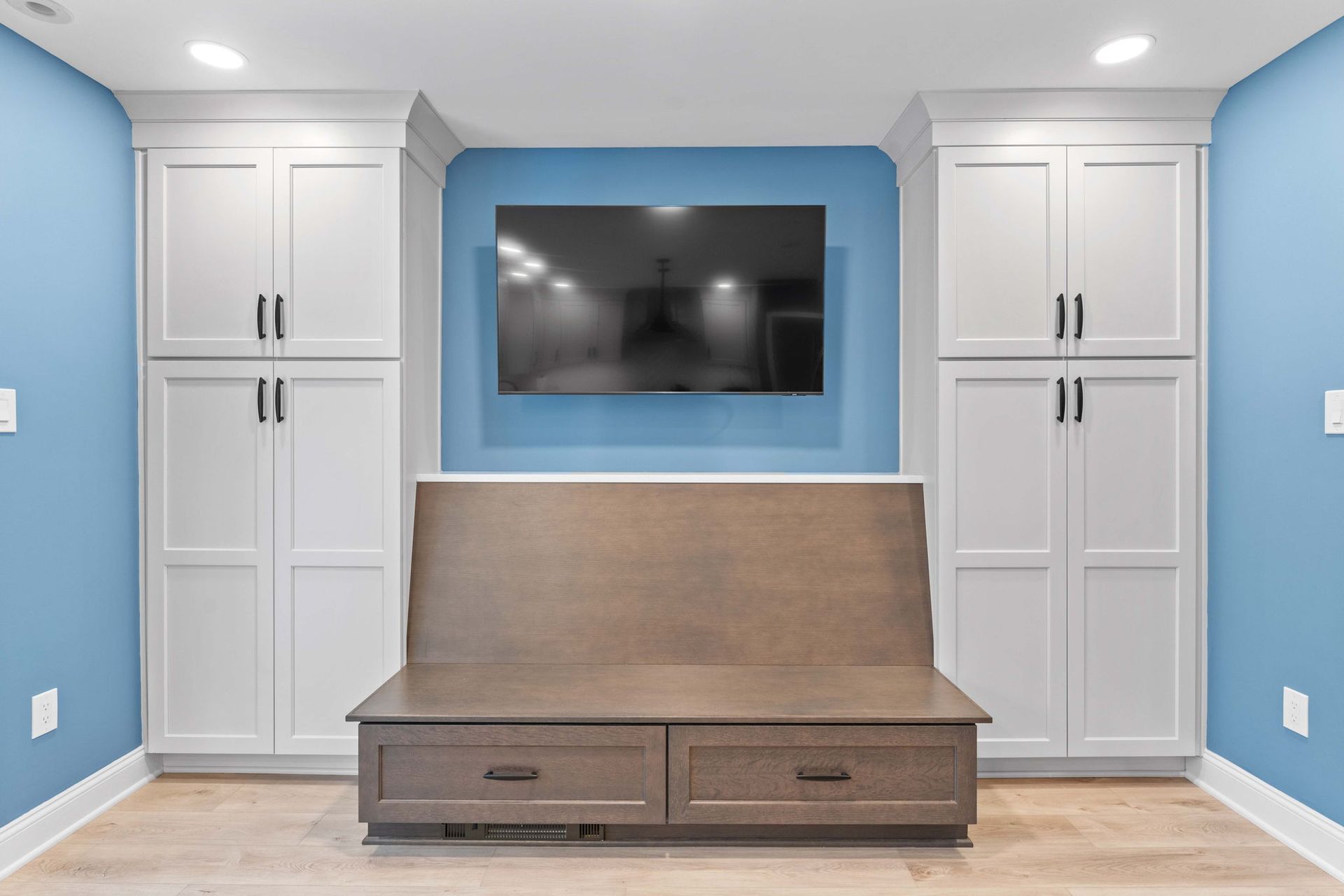 Built-in blue wall with TV, white cabinets, and a wood desk with drawers in a bright room in Bucks County PA
