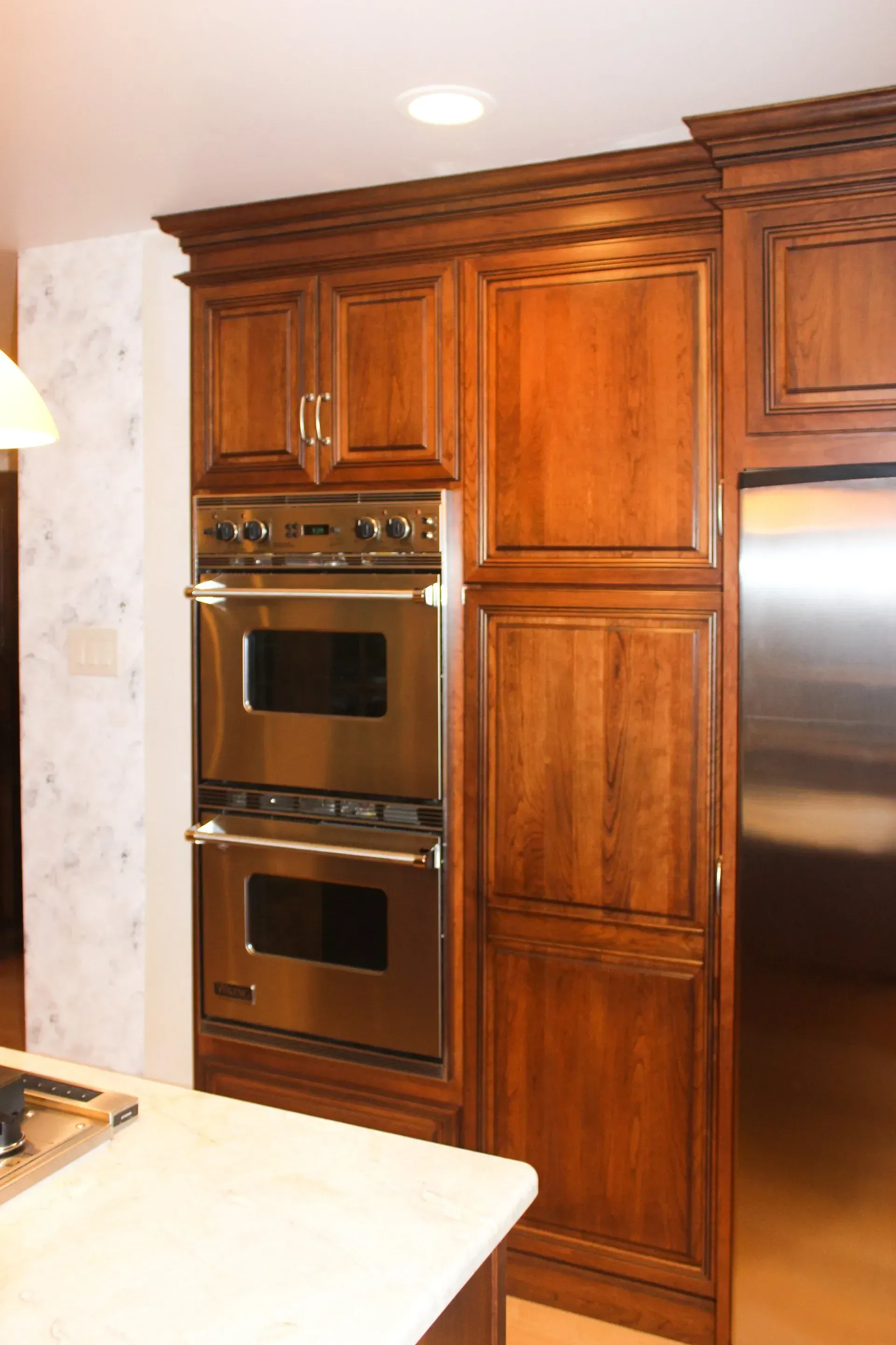 Wooden kitchen cabinets with double wall oven and stainless steel refrigerator beside a countertop In Bucks Country PA