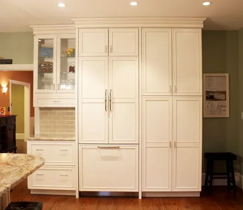 Built-in white kitchen cabinets with glass-front upper doors and pantry storage beside a granite counter In Bucks County PA