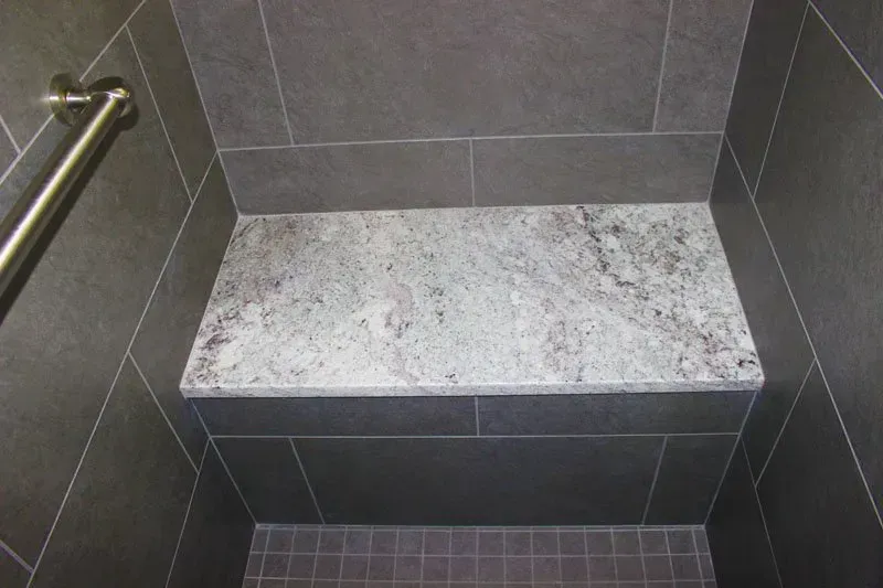 Grey tiled shower bench with a light speckled stone seat and grab bar on the left in Bucks Country PA