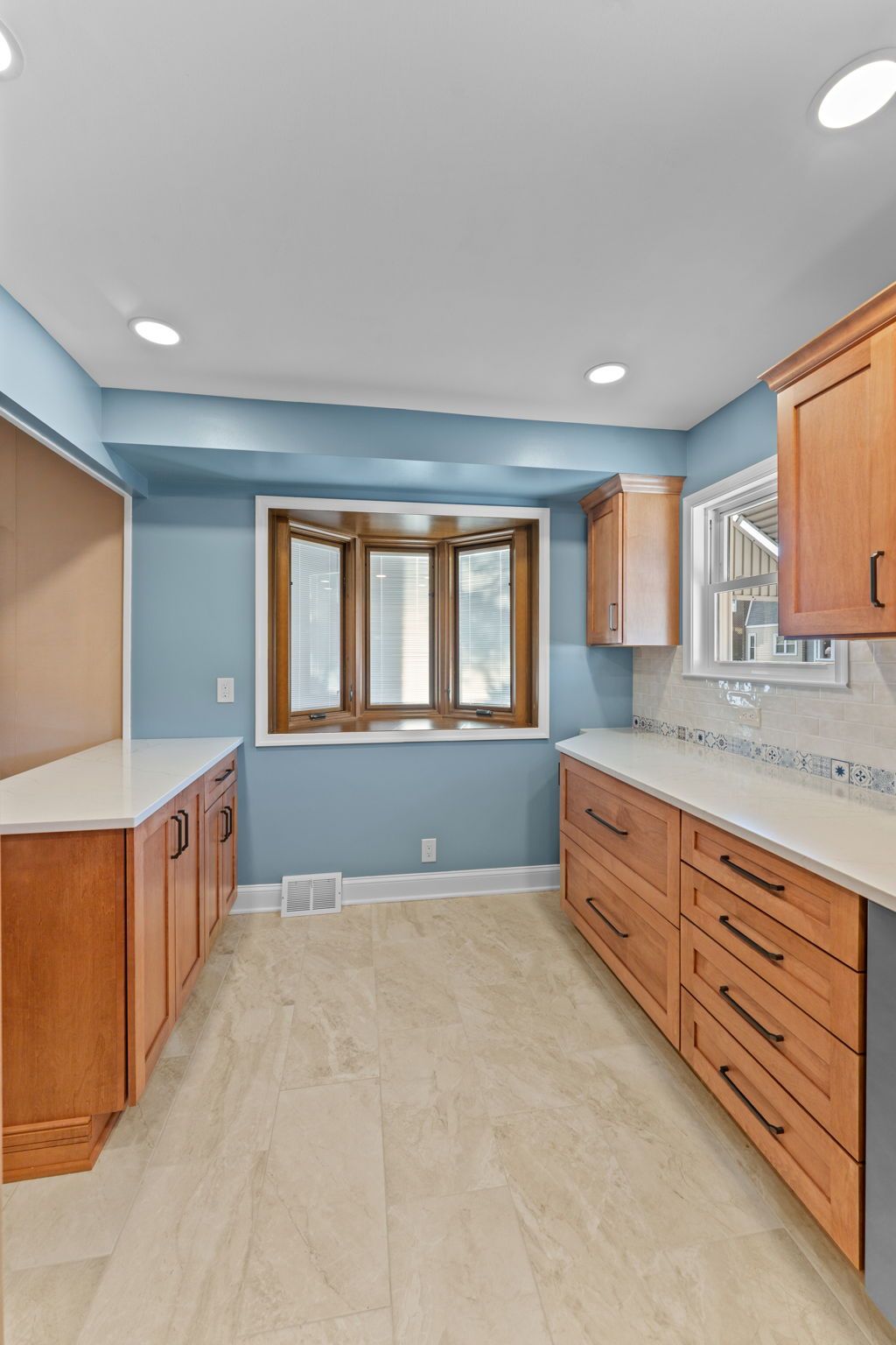 Bright kitchen with blue walls, wood cabinets, light countertops, and a window at the far end In Bucks County PA