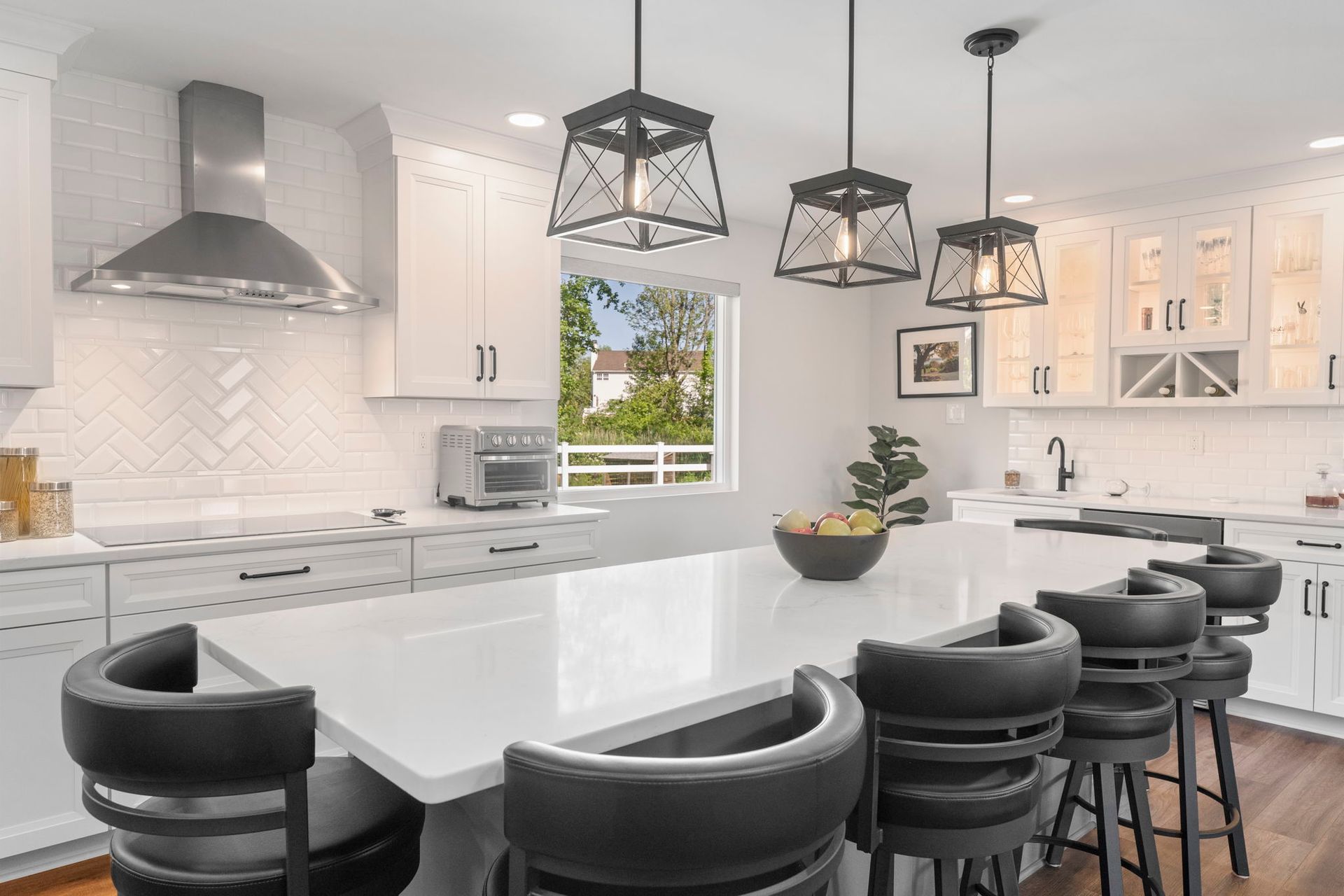 Modern white kitchen with marble island, black bar stools, pendant lights, and stainless steel range hood In Bucks County PA
