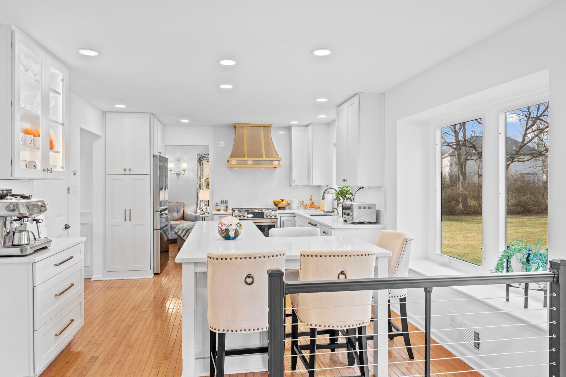 Bright white kitchen with island, wood floors, and a view through large windows to a yard In Bucks Country PA