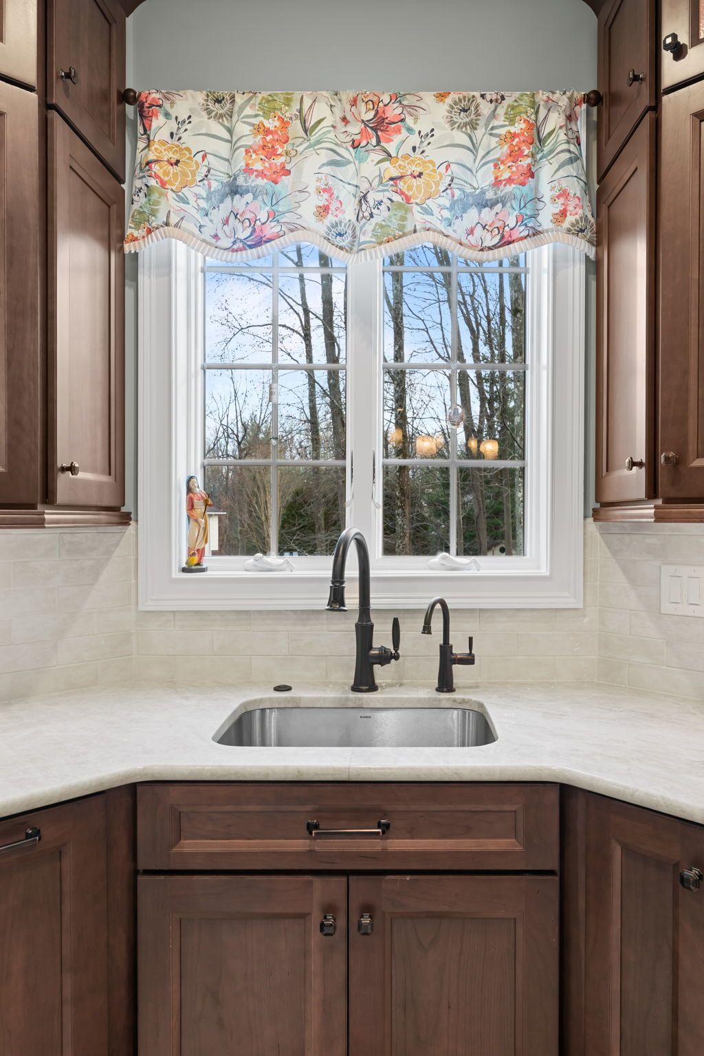 Kitchen sink beneath window with floral valance and dark wood cabinets In Bucks Country PA