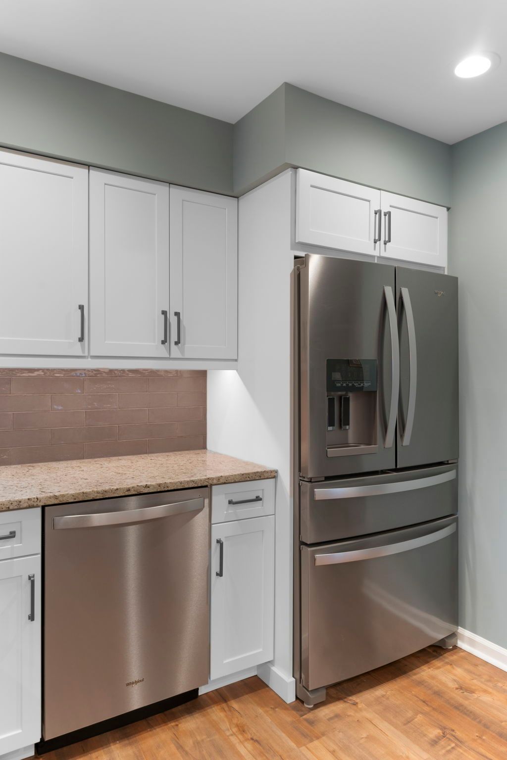 Modern kitchen corner with stainless steel refrigerator and dishwasher, white cabinets, and light countertops In Bucks Country PA