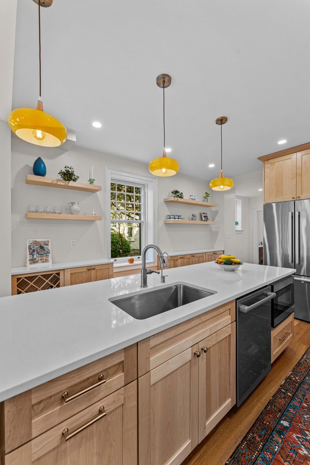 Modern kitchen with white countertops, wood cabinets, yellow pendant lights, and stainless-steel appliances In Bucks County PA