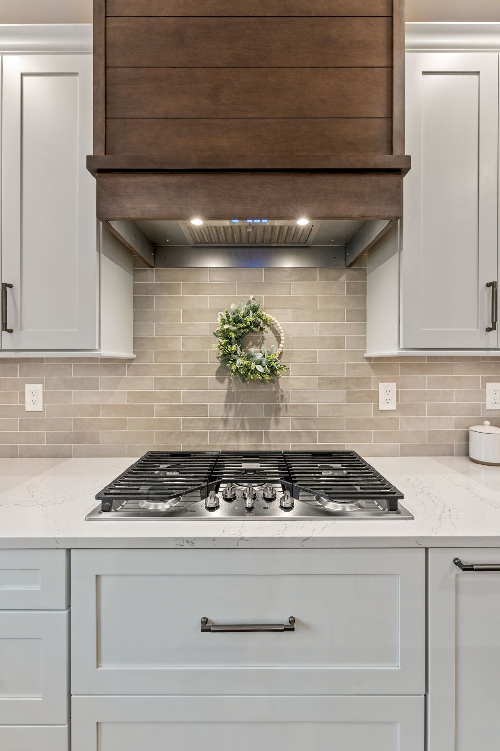 Modern kitchen stovetop with white cabinets, gray backsplash, and wood range hood  In Bucks County PA