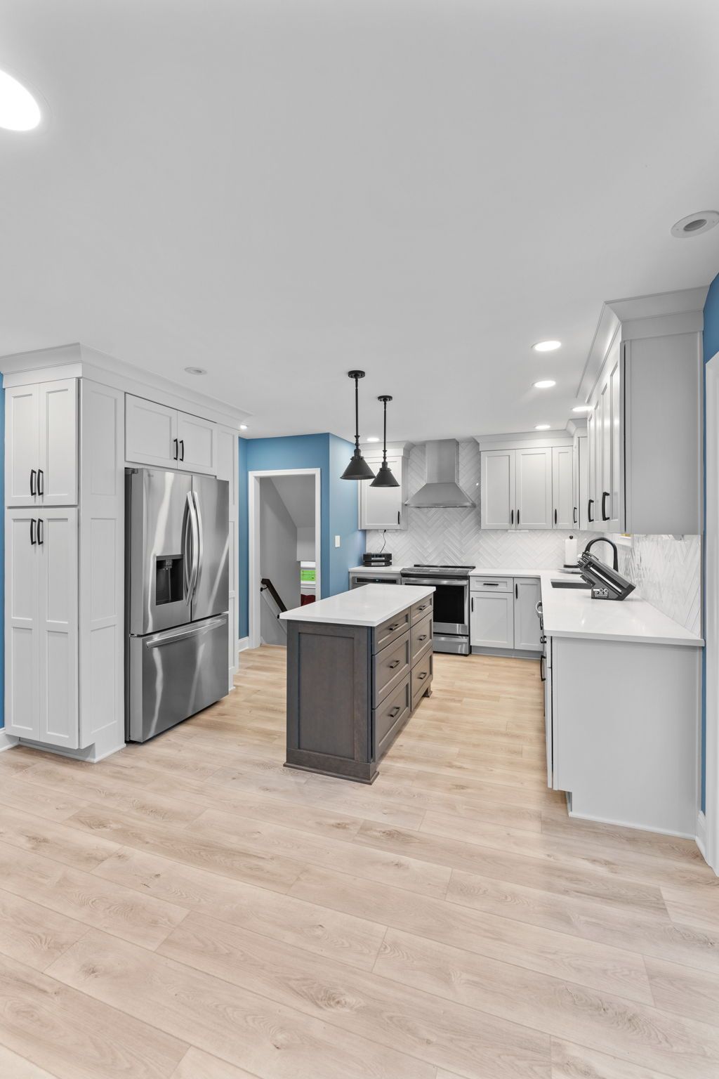 Bright modern kitchen with white cabinets, stainless appliances, and a dark island with pendant lights In Bucks Country PA