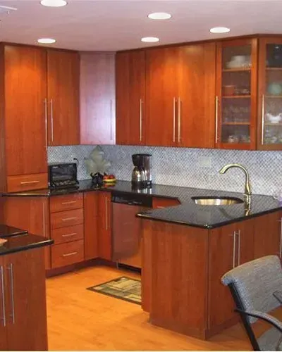 Modern kitchen with cherry wood cabinets, black countertops, stainless sink, and a tiled backsplash In Bucks Country PA