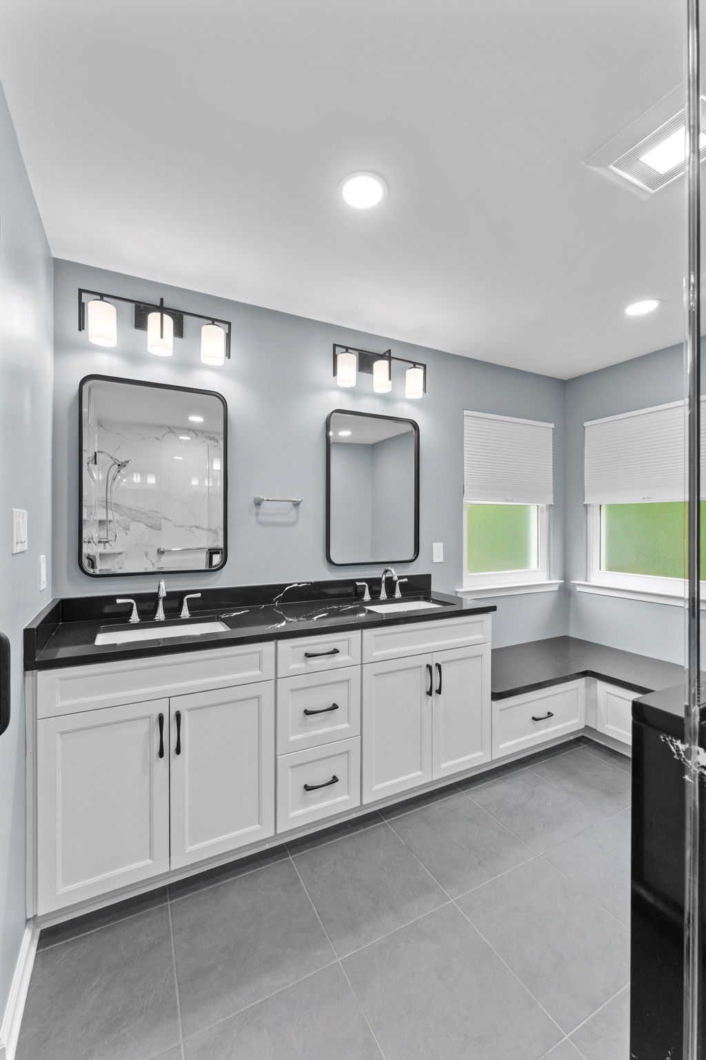 Modern white bathroom with double vanity, black countertops, mirrors, and large windows with blinds  In Bucks County PA
