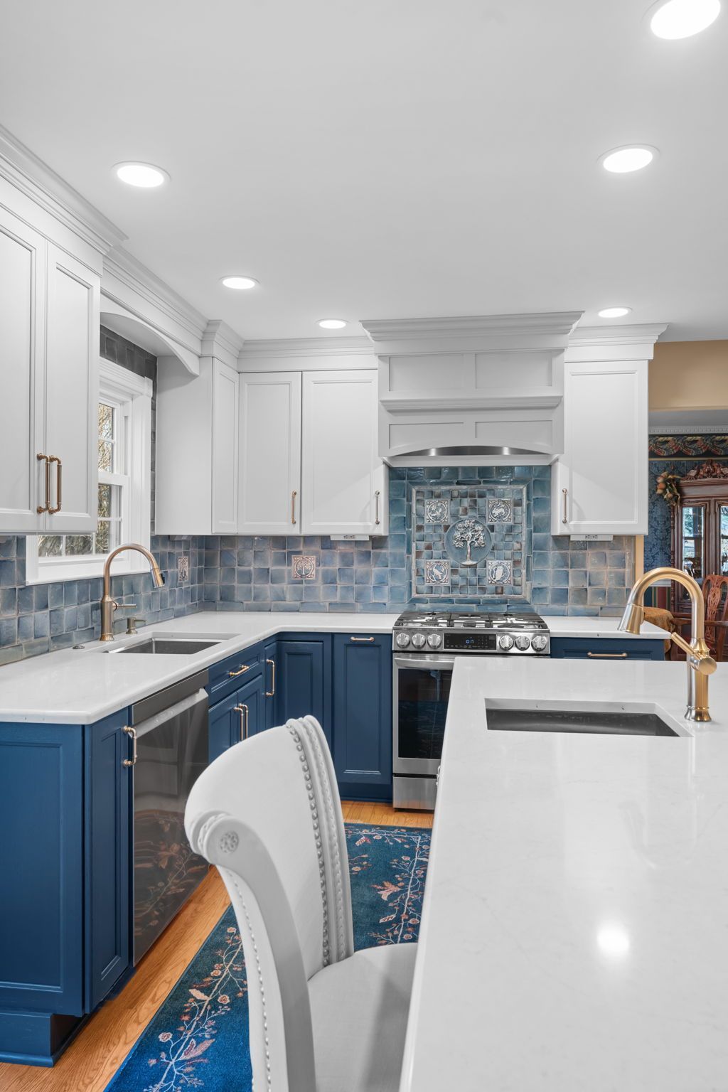 Bright white and blue kitchen with island, barstools, stainless stove, and recessed ceiling lights  In Bucks County PA
