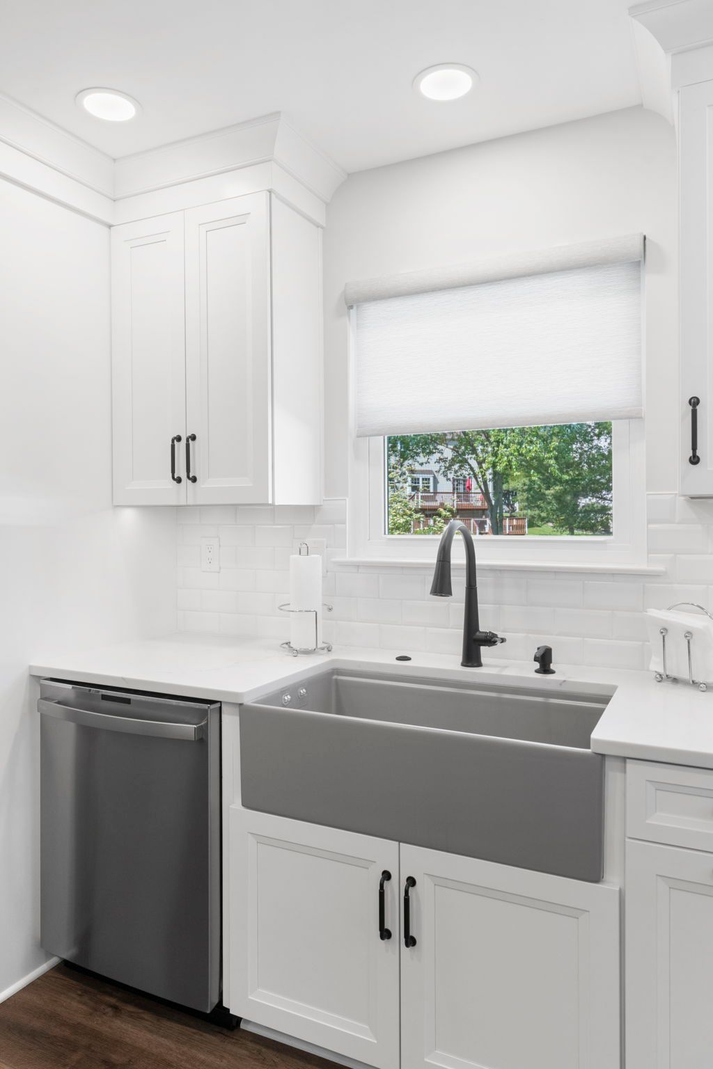 Bright white kitchen sink with gray farmhouse basin, black faucet, window, dishwasher, and white cabinets In Bucks County PA