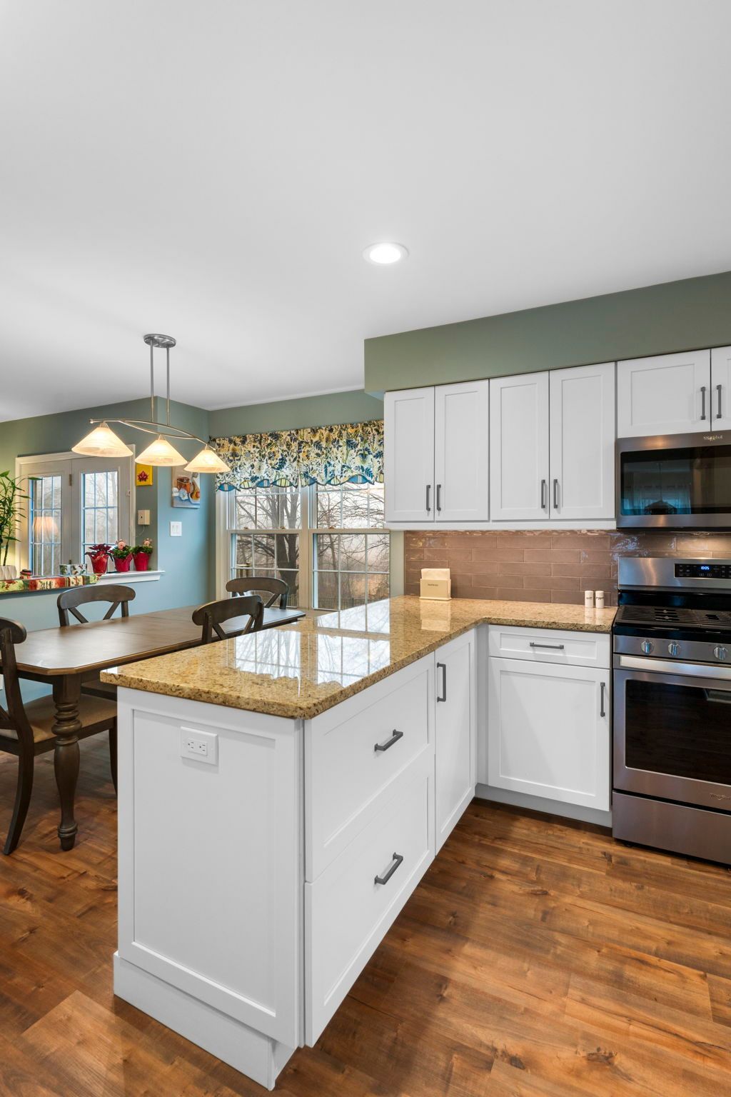 Bright kitchen with white cabinets, granite island, stainless oven, and wood floors opening to a dining area In Bucks Country PA