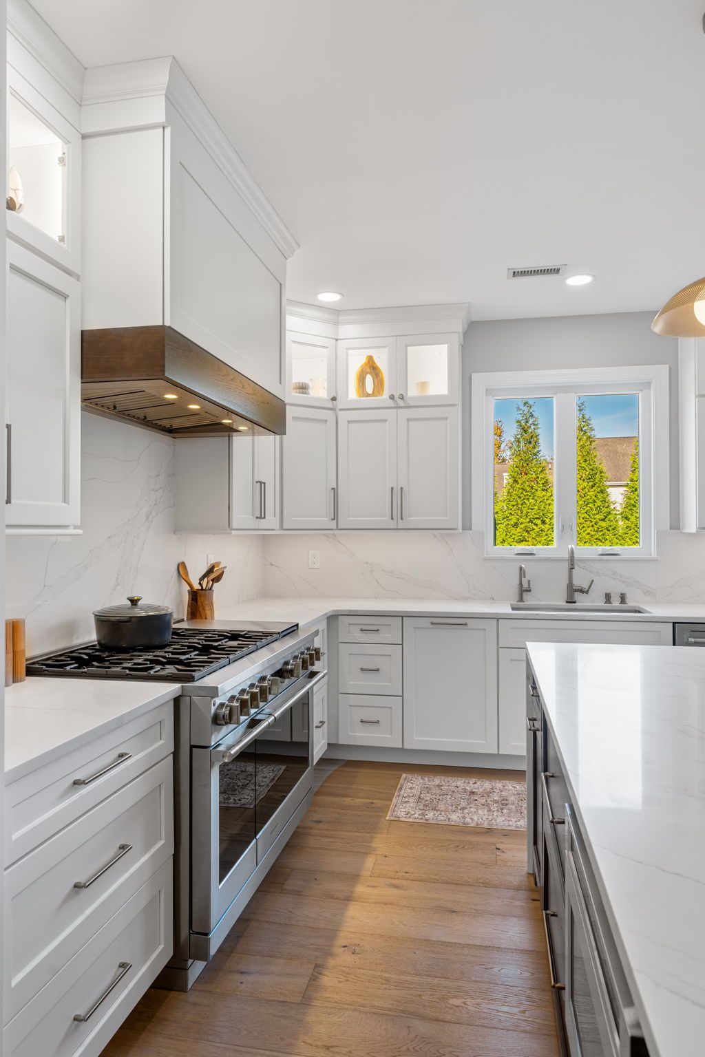 Bright white modern kitchen with stainless stove, wood floor, and sunny window above the sink In Bucks Country PA