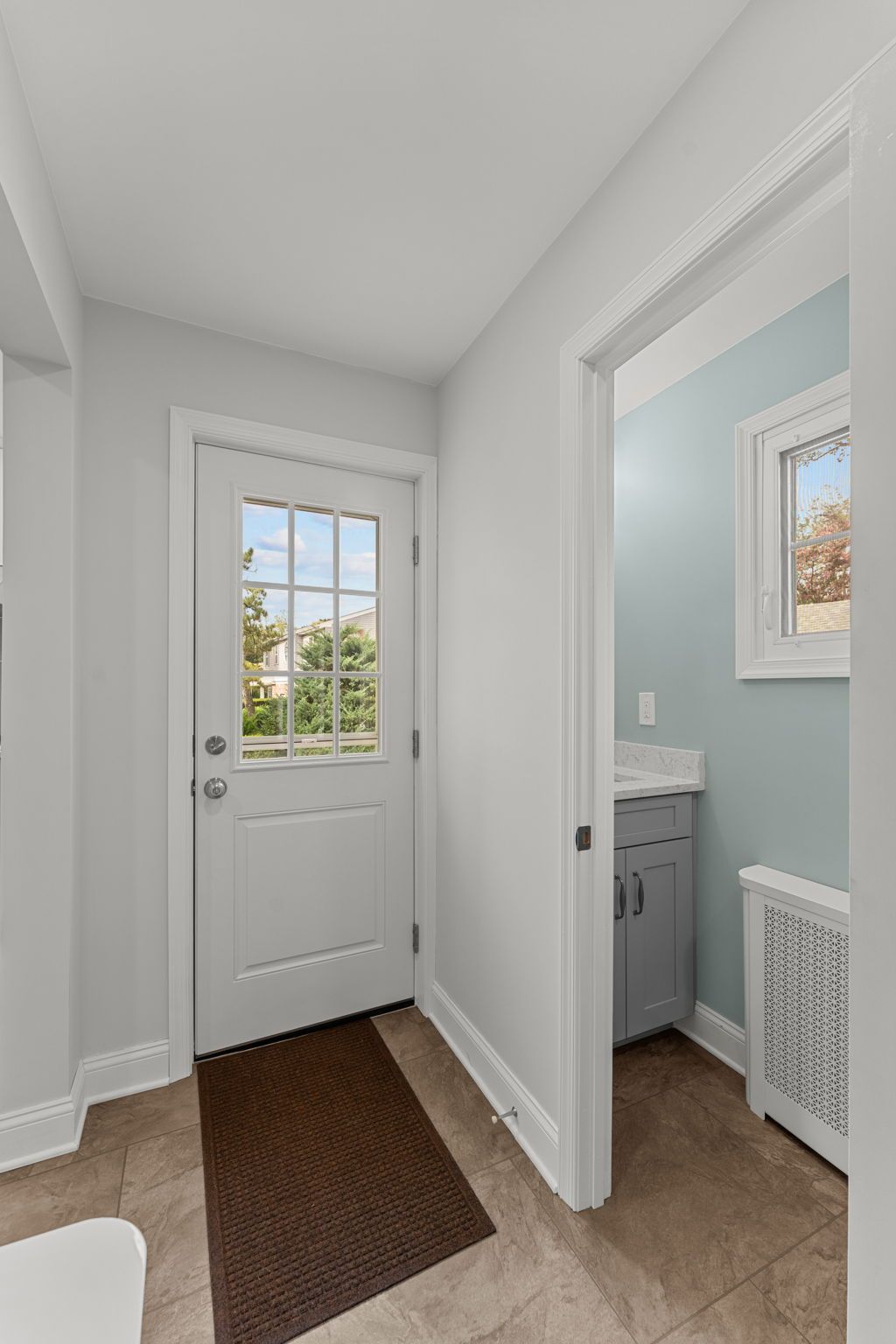 Bright hallway with white walls, front door, brown rug, and open bathroom door to the right in Bucks County PA