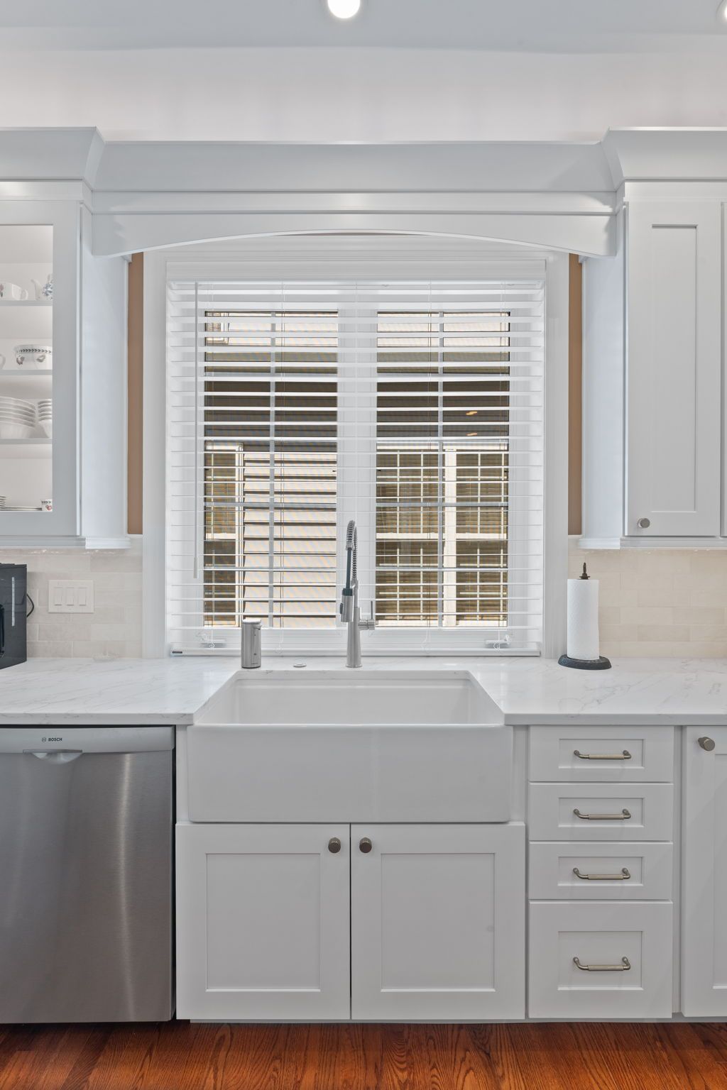 White kitchen sink under a window with shutters, surrounded by white cabinets and stainless dishwasher. In Bucks County PA
