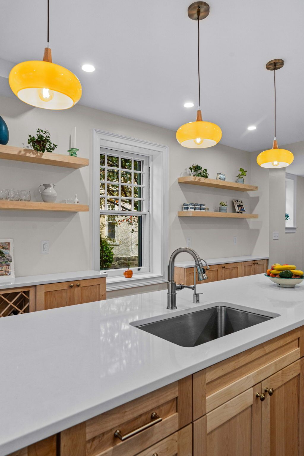 Modern kitchen with white countertops, wood cabinets, open shelves, pendant lights, and a double sink In Bucks County PA