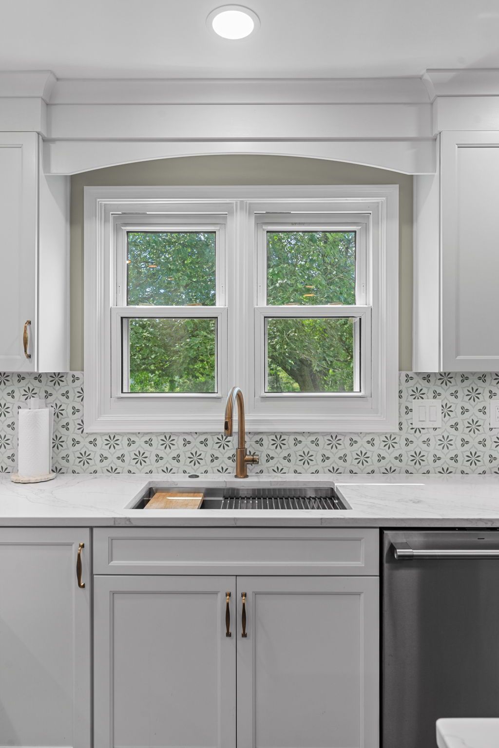 Bright white kitchen with a window over a sink, gray cabinets, and a patterned tile backsplash In Bucks County PA