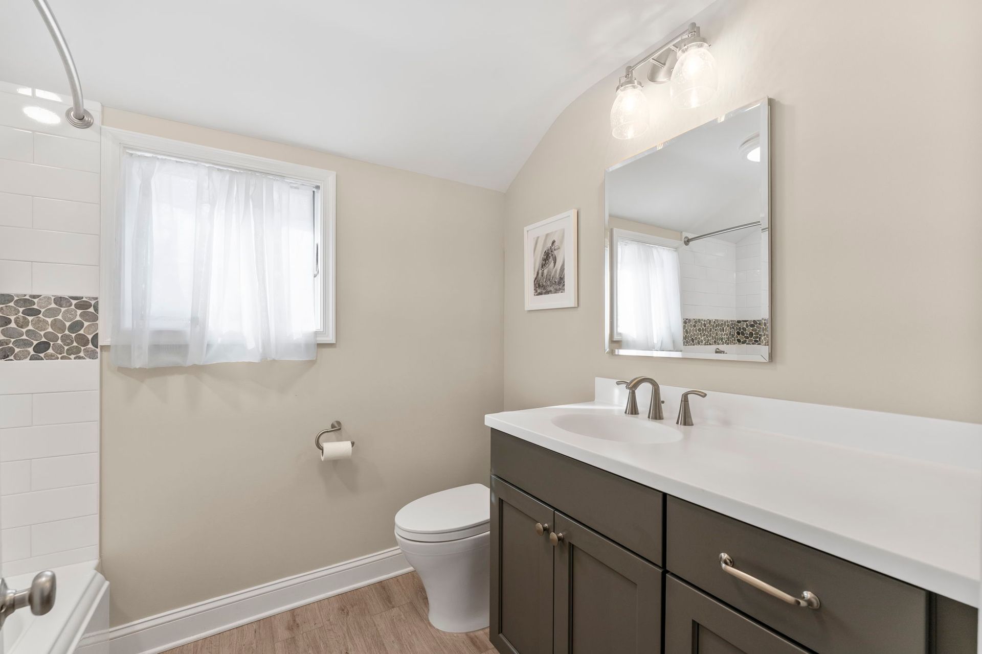 Bright bathroom with white vanity, mirror, toilet, window, and tiled shower wall  In Bucks County PA