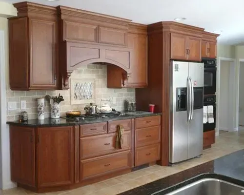 Wooden kitchen cabinets and stainless steel refrigerator with black countertops and tiled backsplash In Bucks Country PA