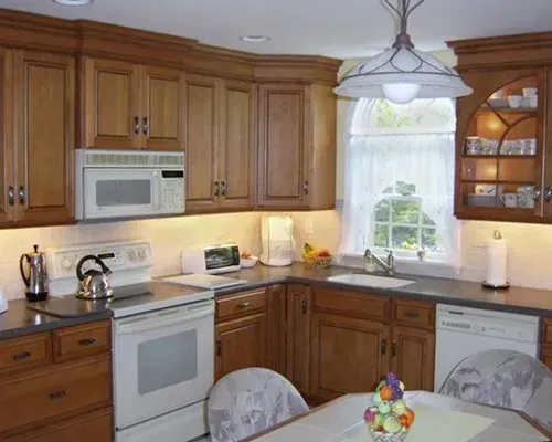 Bright kitchen with wood cabinets, white appliances, sink by window, and dining table in foreground In Bucks Country PA