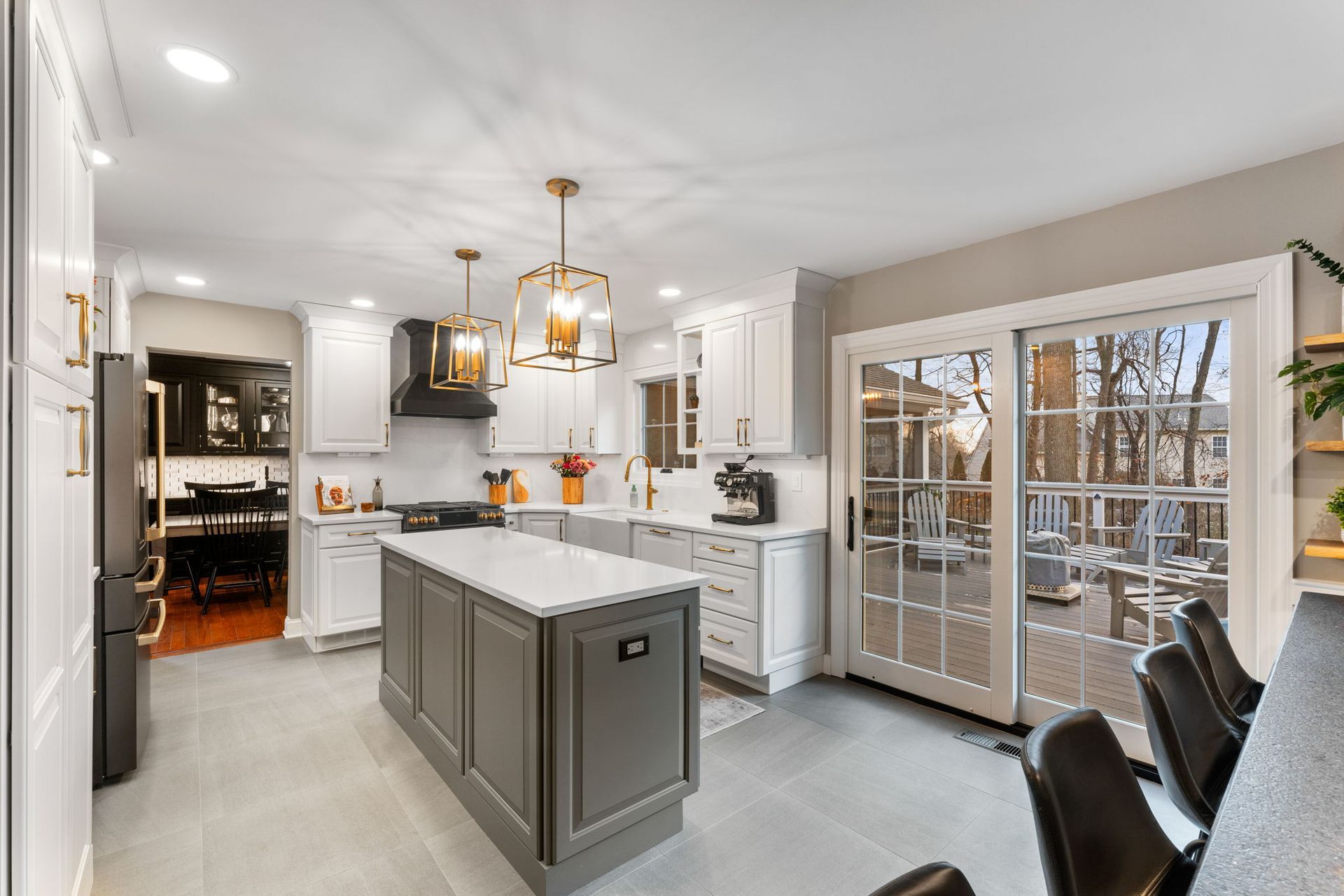 Bright modern kitchen with gray island, white cabinets, gold pendant lights, and glass doors to a deck In Bucks Country PA