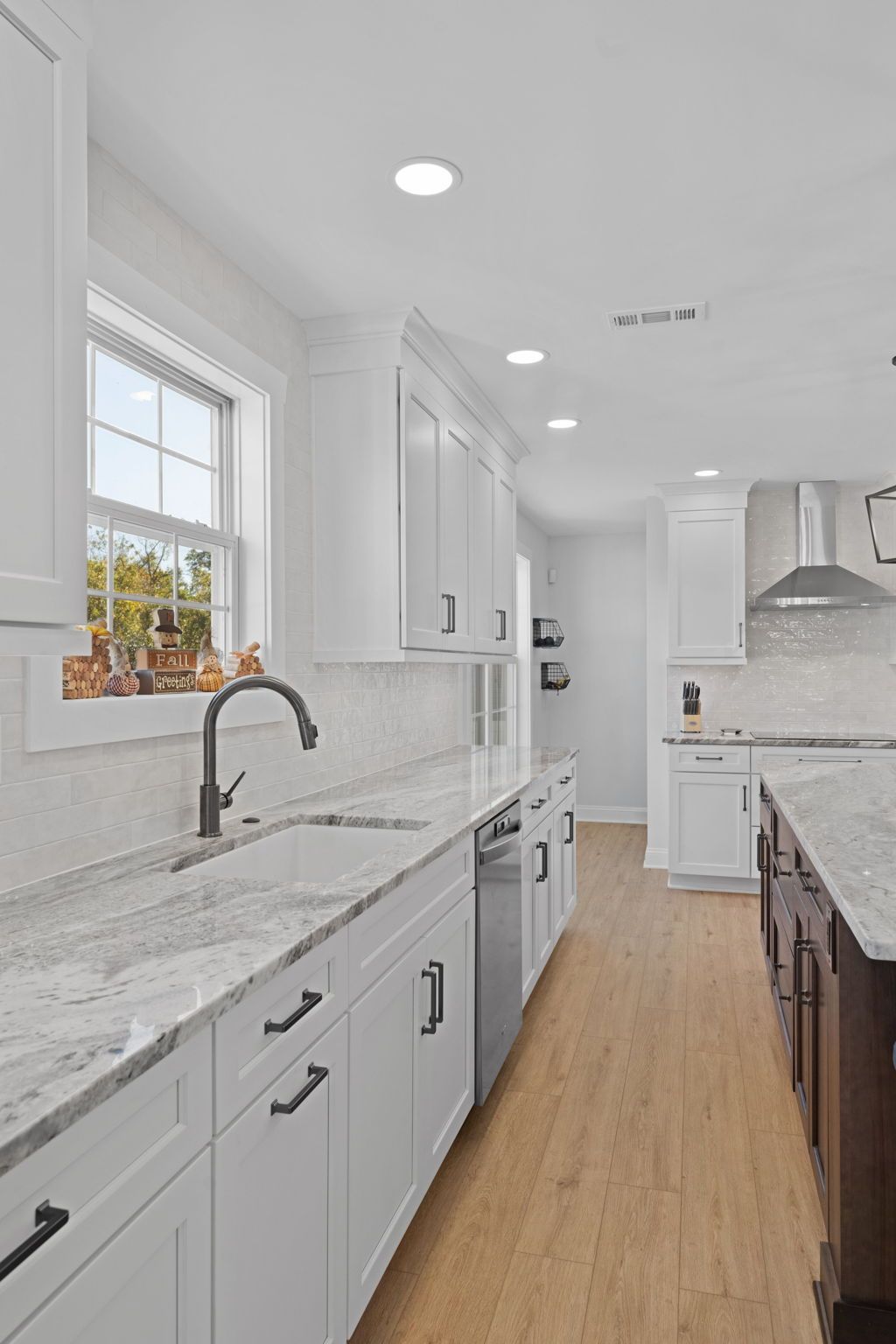 Bright modern kitchen with white cabinets, marble countertops, wood floors, and a window over the sink  In Bucks County PA