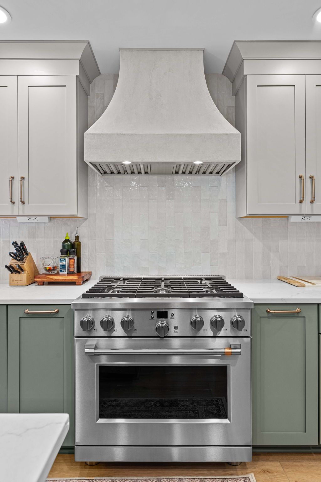 Modern kitchen with stainless steel stove, white hood, and sage green lower cabinets in Bucks County PA