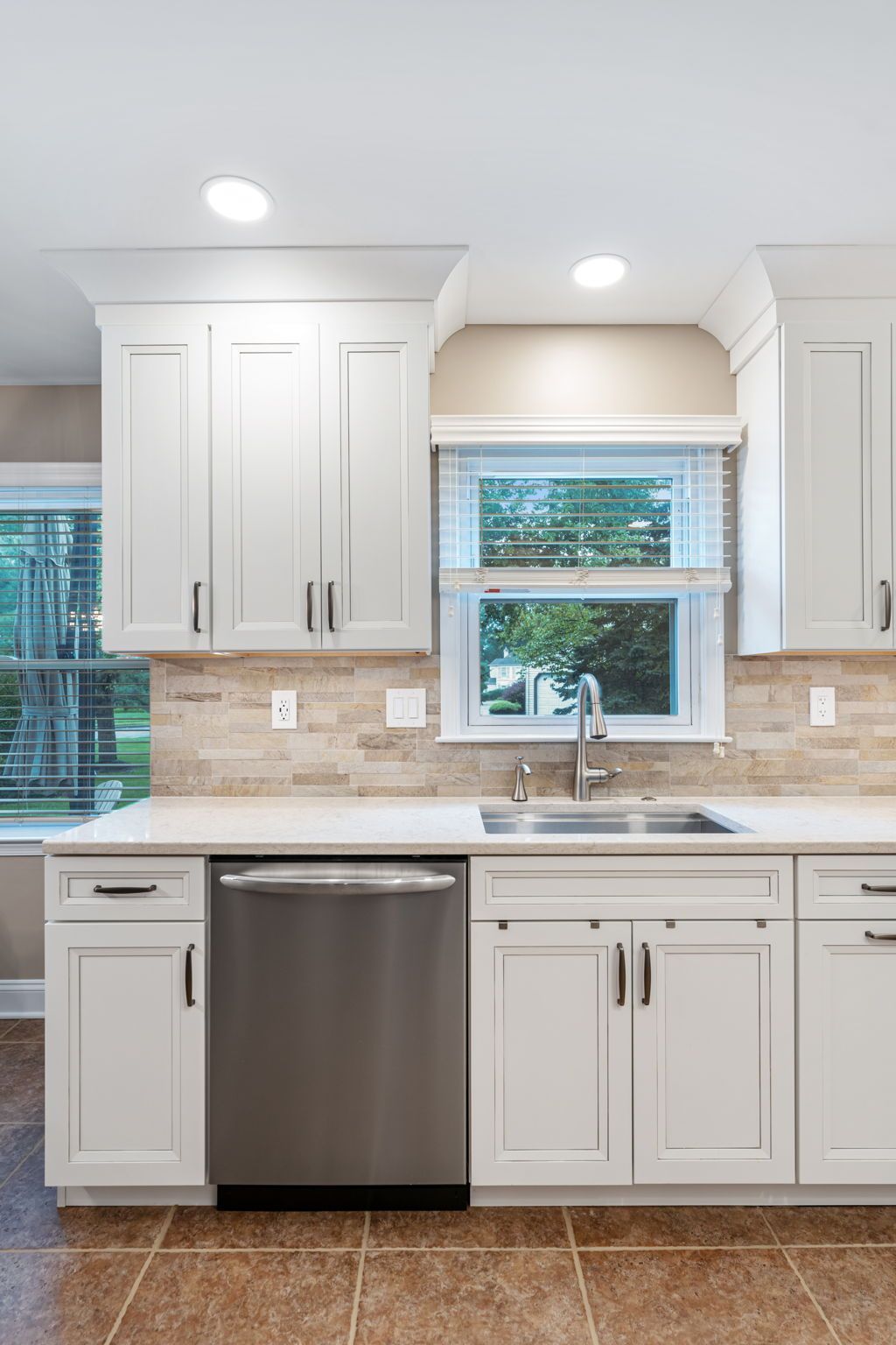 Bright white kitchen with stainless dishwasher, double sink under window, and recessed ceiling lights In Bucks County PA
