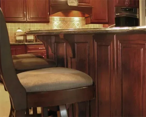 Wooden bar stools at a polished kitchen island with warm brown cabinets and tile backsplash  In Bucks County PA