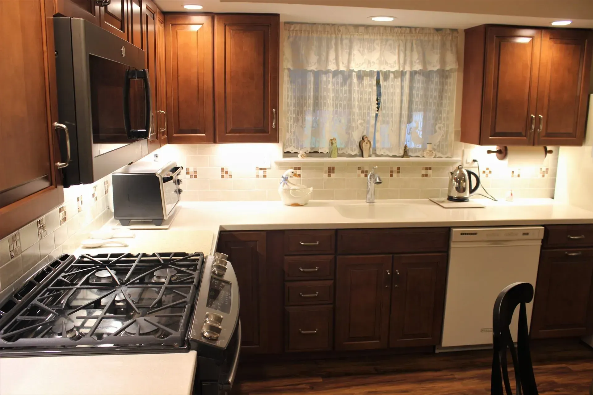 Kitchen with wooden cabinets, white countertops, and a stainless steel stove under warm lighting In Bucks Country PA