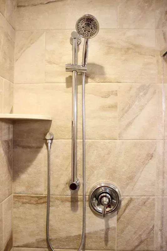 Shower with handheld showerhead and wall-mounted control on beige tiled bathroom wall In Bucks Country PA