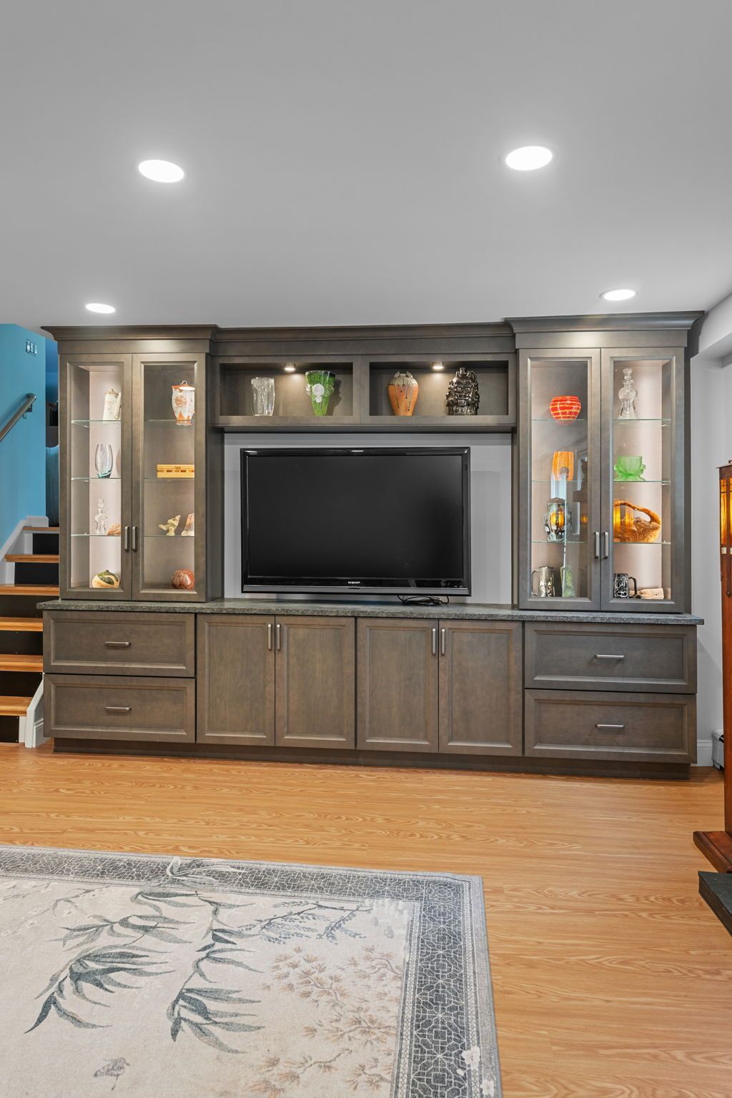 Living room wall unit with TV, dark wood cabinets, glass display shelves, and recessed lights In Bucks County PA