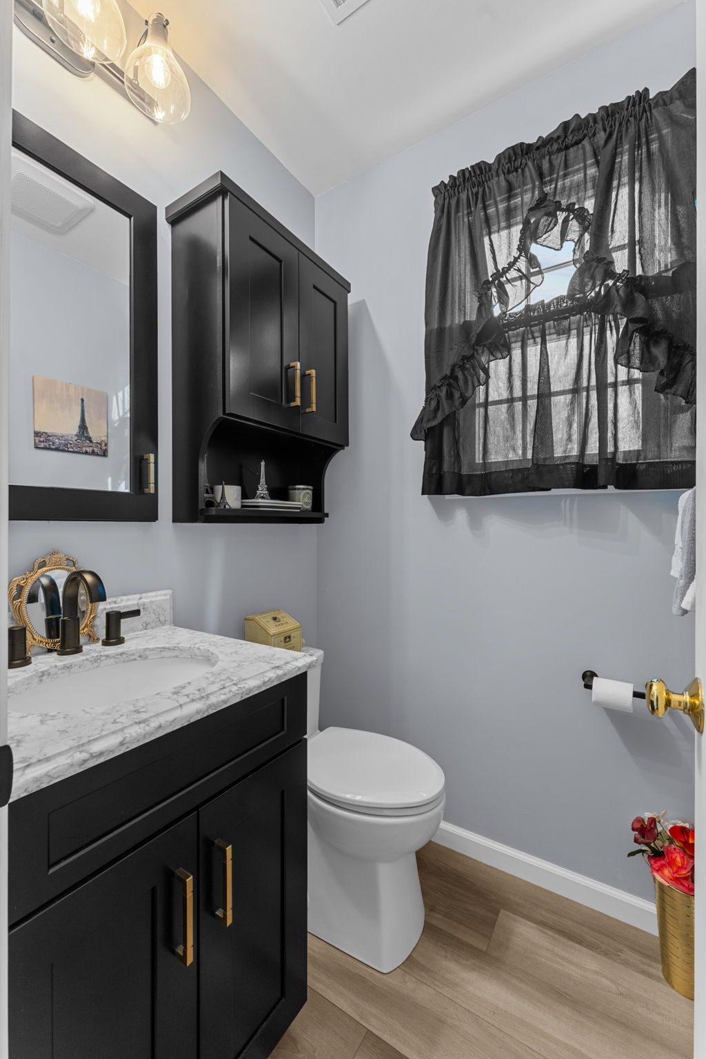 Small bathroom with black vanity, white toilet, gray walls, and a window with black curtains In Bucks Country PA