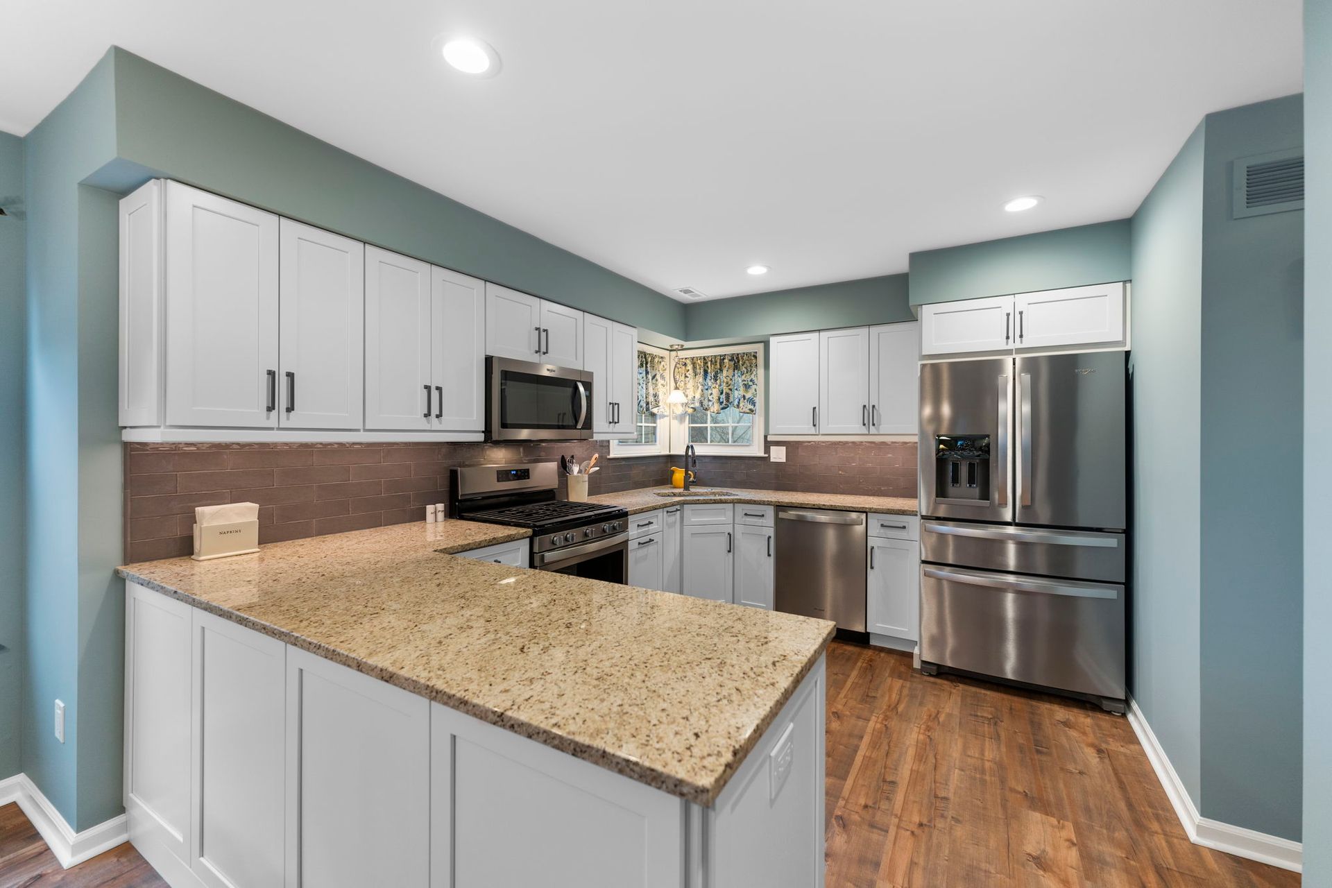 Bright modern kitchen with white cabinets, granite countertops, stainless steel appliances, and teal walls In Bucks Country PA