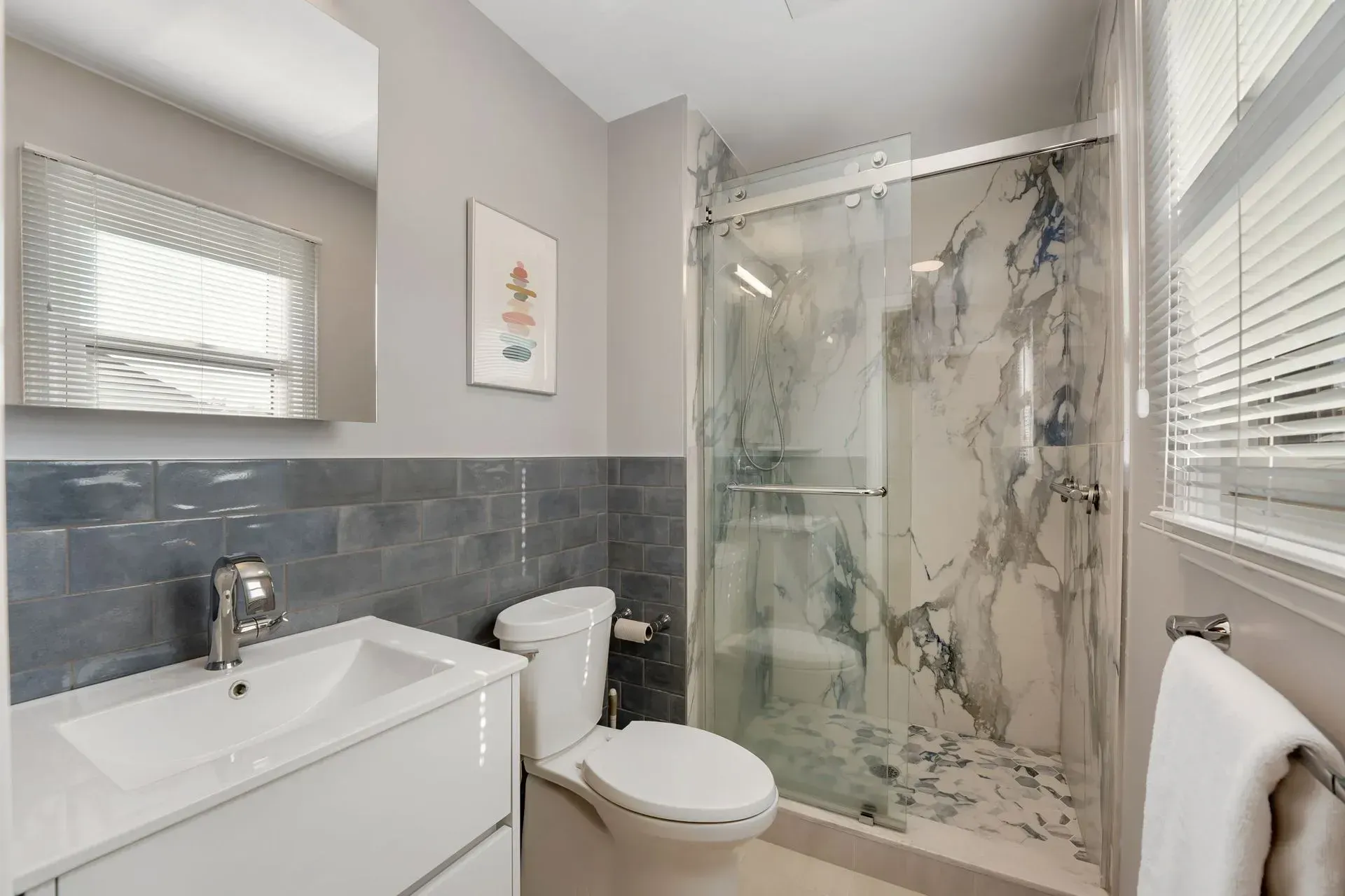 Bright modern bathroom with glass shower, toilet, white vanity, and gray tile accents  In Bucks County PA