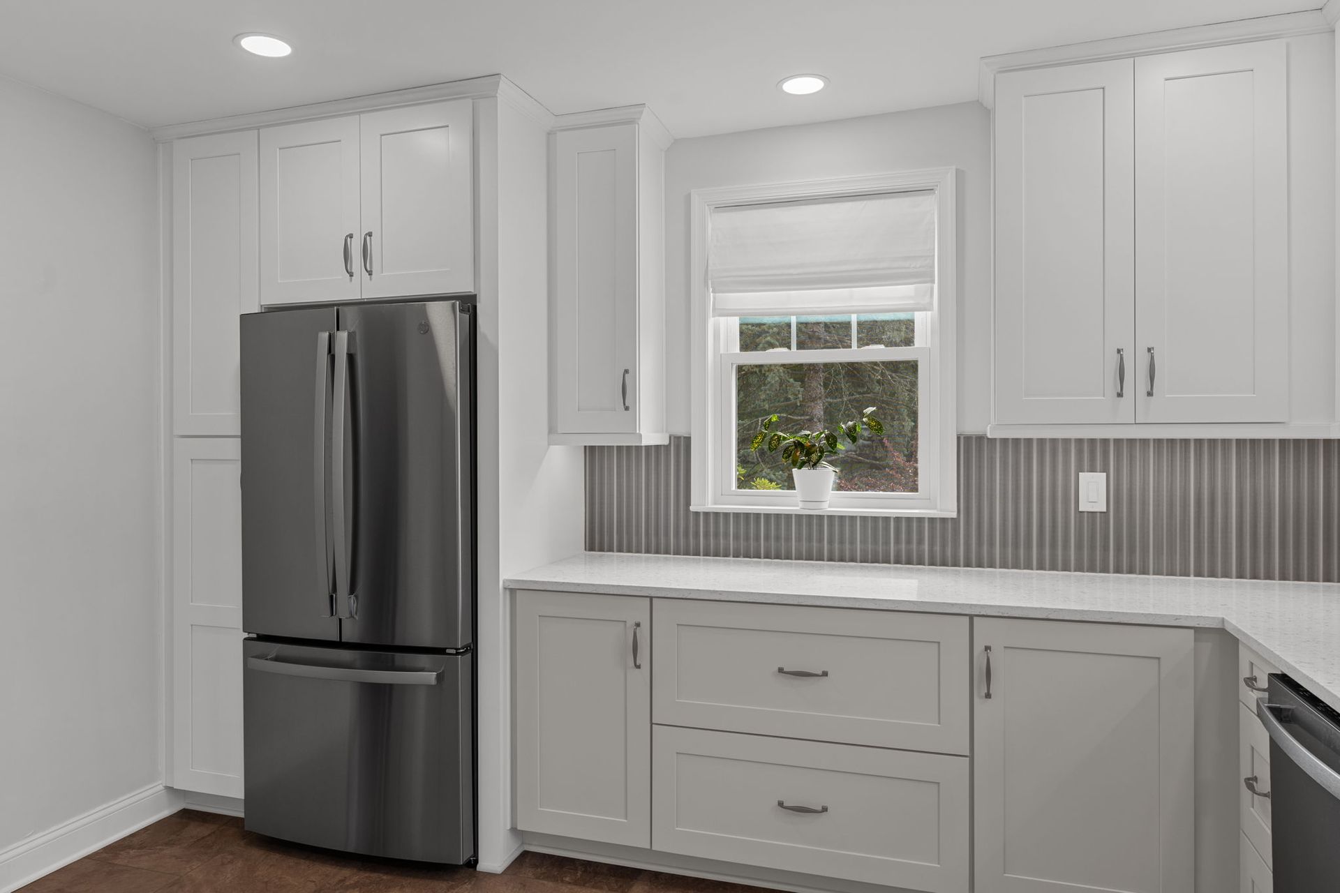 Bright kitchen with stainless steel fridge, white cabinets, gray backsplash, and a window over the sink In Bucks County PA