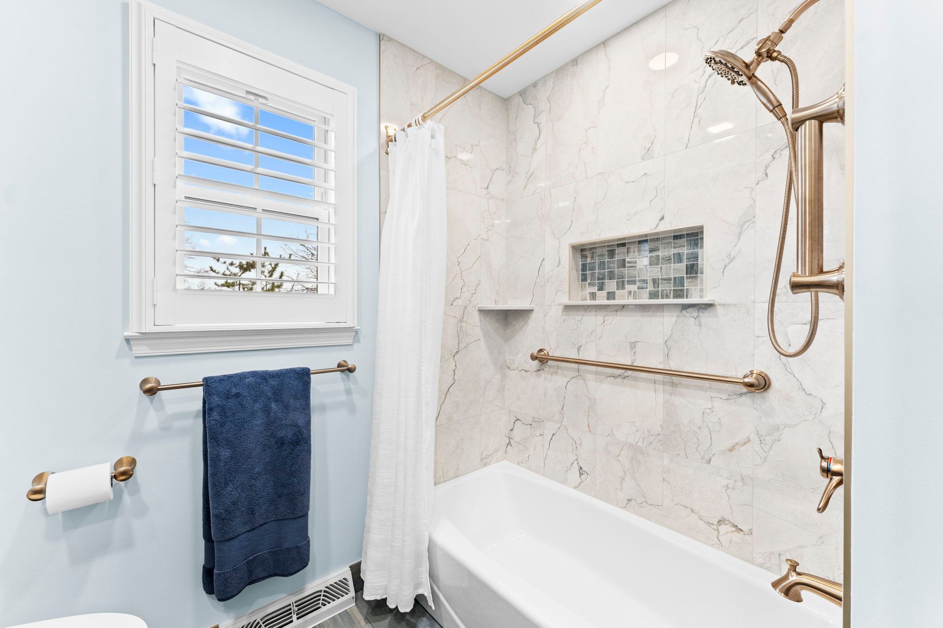 Bright bathroom with marble tile, white tub, gold fixtures, and a blue towel by the windowIn Bucks County PA
