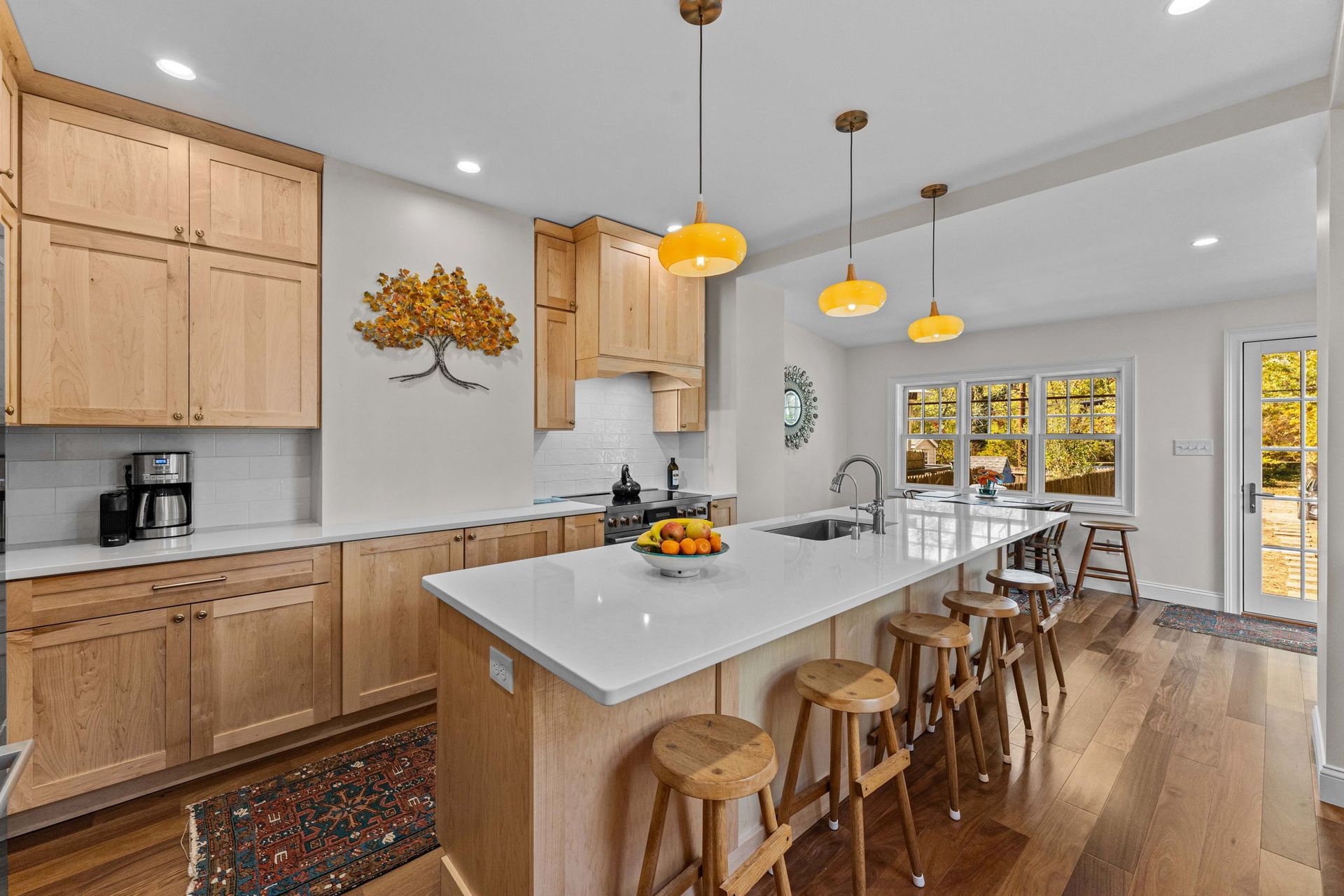 Bright modern kitchen with wood cabinets, white island, pendant lights, and stools by a windowed dining area In Bucks County PA