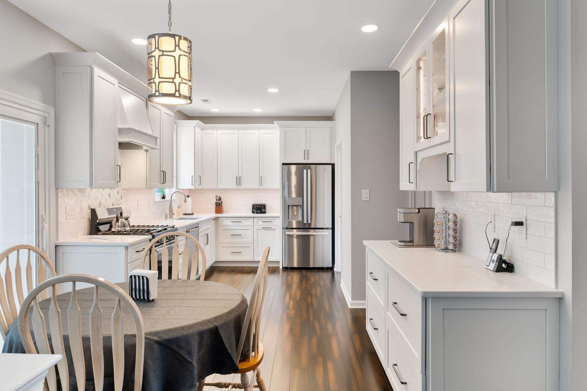 Bright white kitchen with island, stainless fridge, wood floors, and a dining table in the foreground In Bucks Country PA