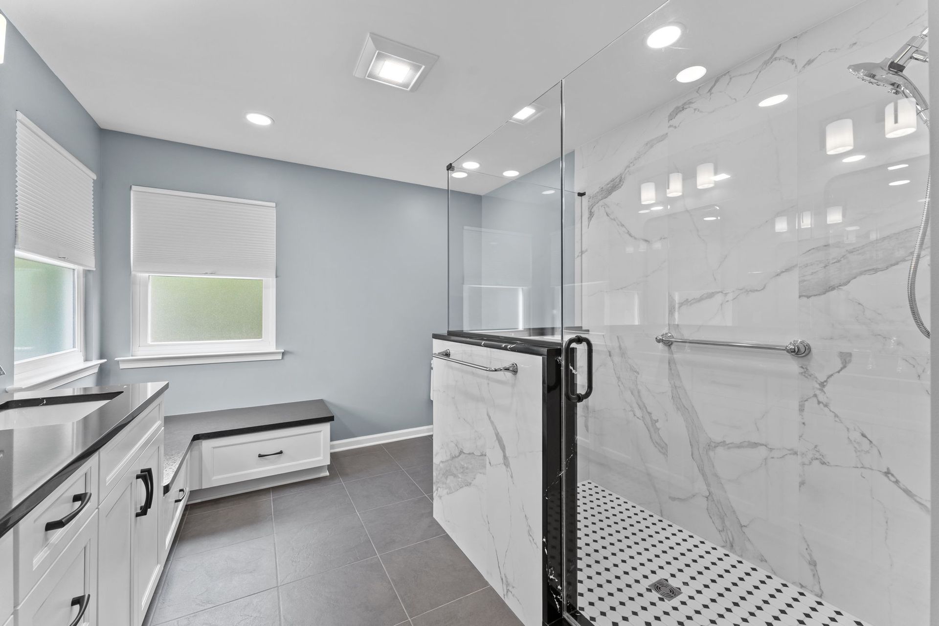 Modern bathroom with white marble shower, double vanity, gray walls, and a bench by the window In Bucks County PA