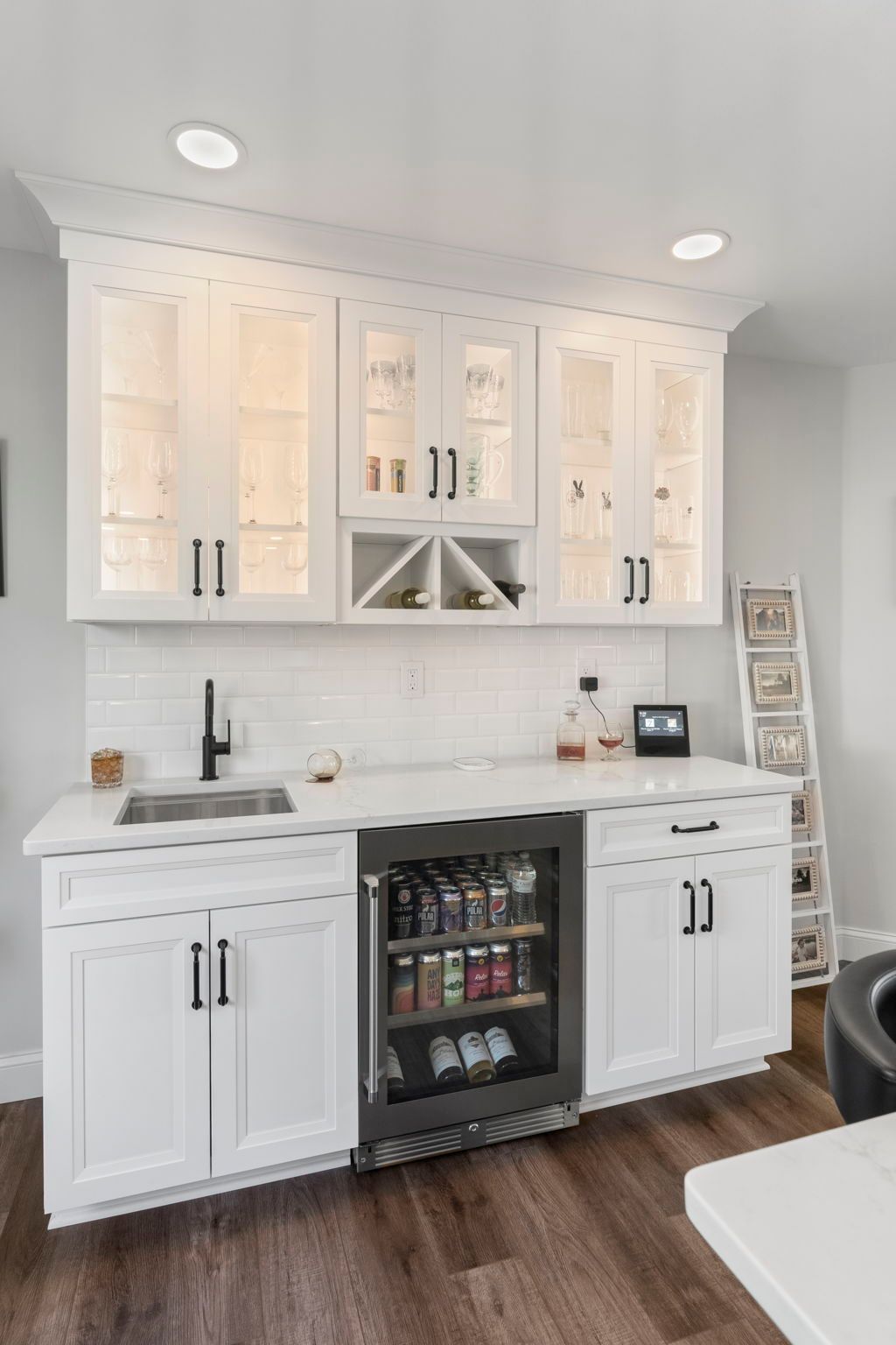 White home bar with cabinets, sink, and mini fridge against a white wall and wood floor In Bucks County PA
