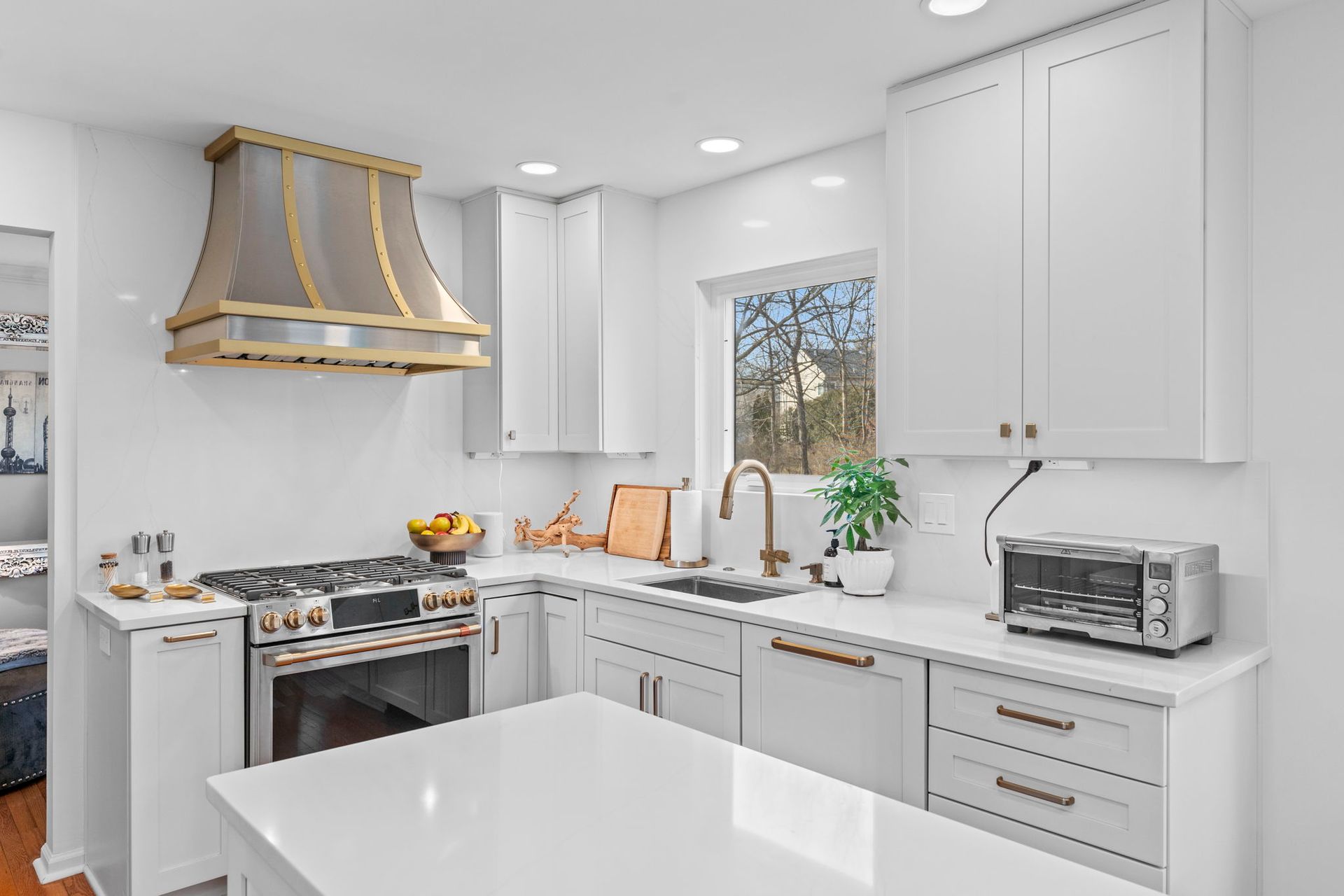 Bright white modern kitchen with island, gray cabinets, gold range hood, and window over sink