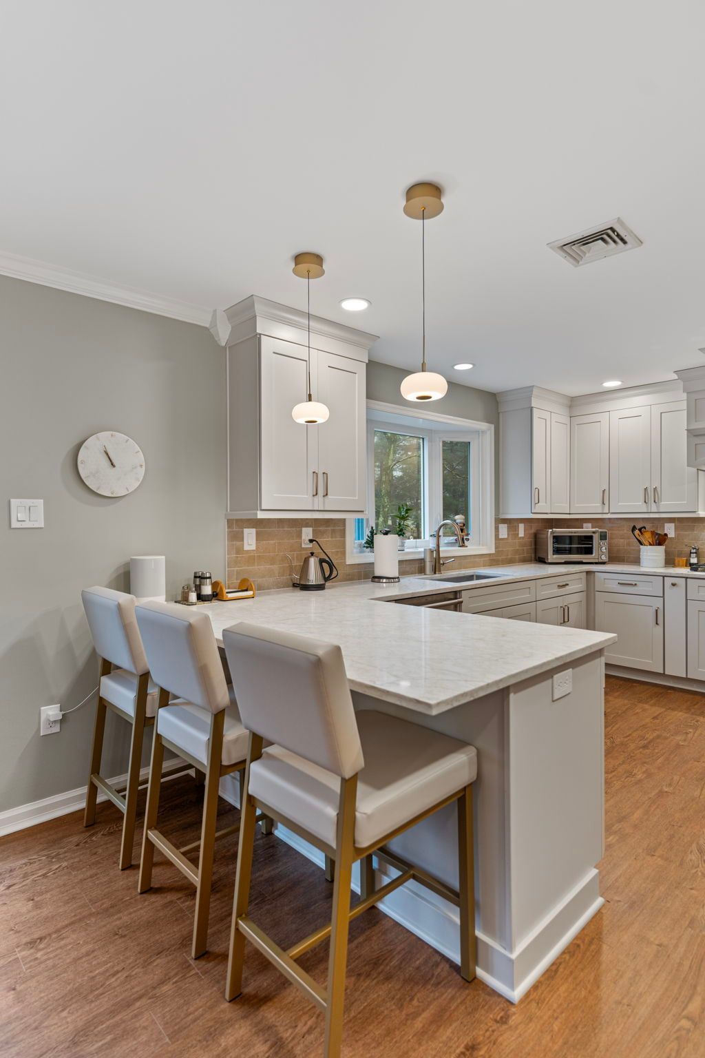 Bright modern kitchen with white cabinets, marble island, pendant lights, and four bar stools In Bucks County PA