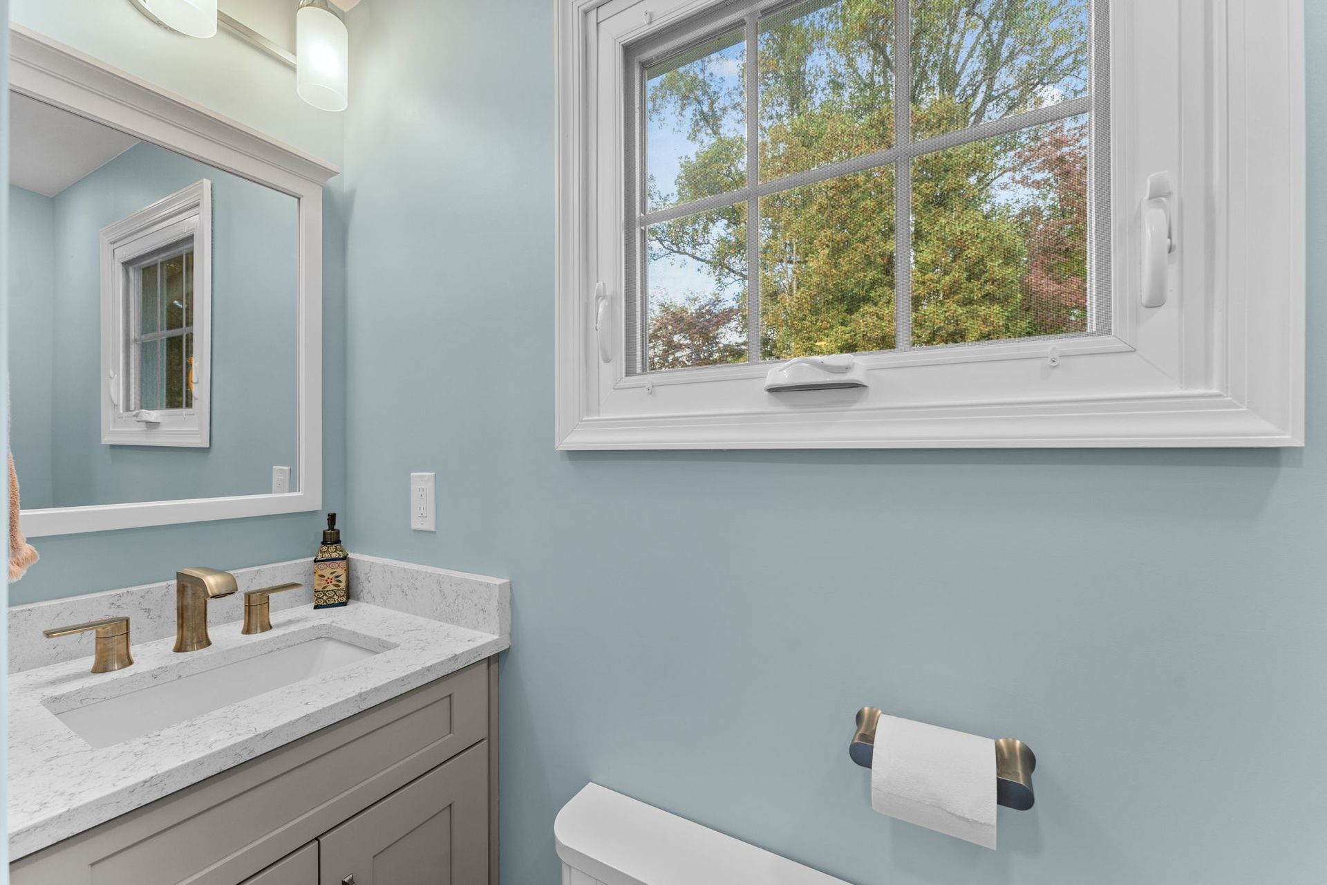 Light blue bathroom with white vanity, mirror, window, and towel rack in Bucks County PA