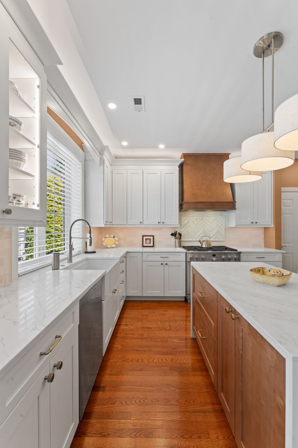 Modern white kitchen with wood cabinets, marble counters, pendant lights, and hardwood floor In Bucks County PA