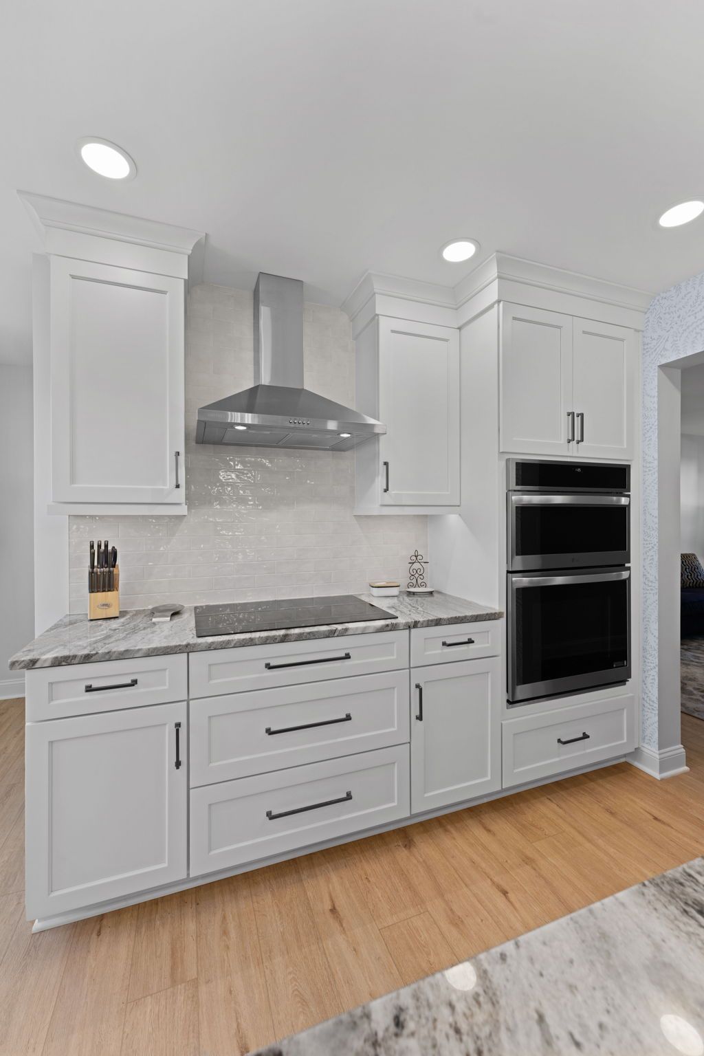 Modern white kitchen with marble backsplash, stainless range hood, and double wall ovens  In Bucks County PA