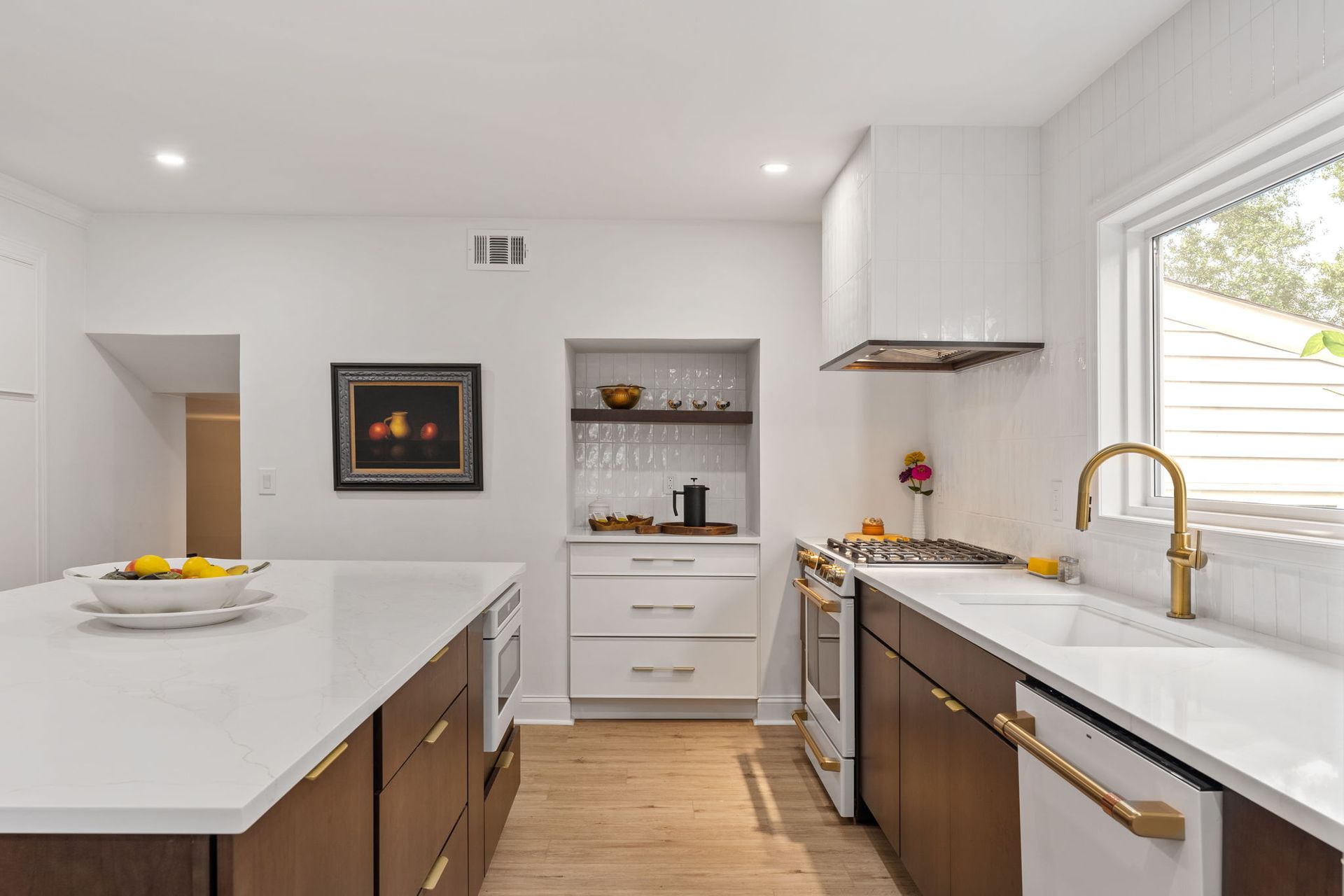 Bright modern kitchen with white island, gold faucet, and built-in oven beside a dining nook In Holland PA