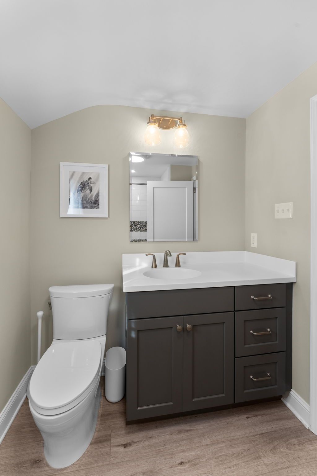 Small bathroom with toilet, dark vanity, white sink, mirror, and framed wall art Hatboro Bath Bucks County PA