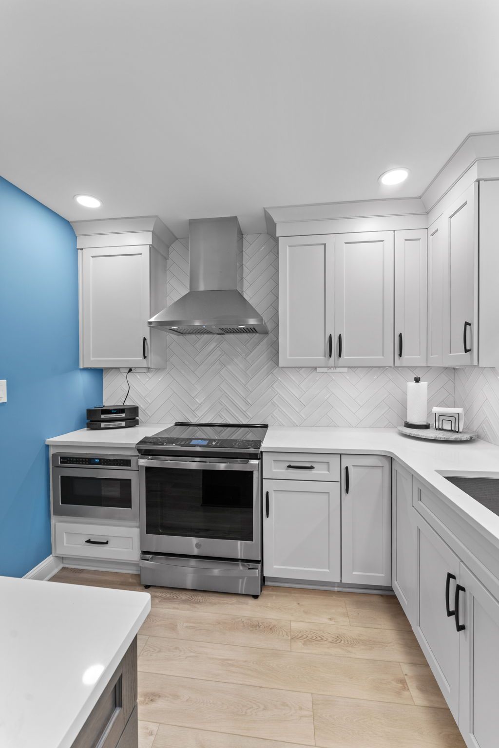 Bright white kitchen with blue accent wall, stainless steel stove, and light wood floor in Bucks County PA